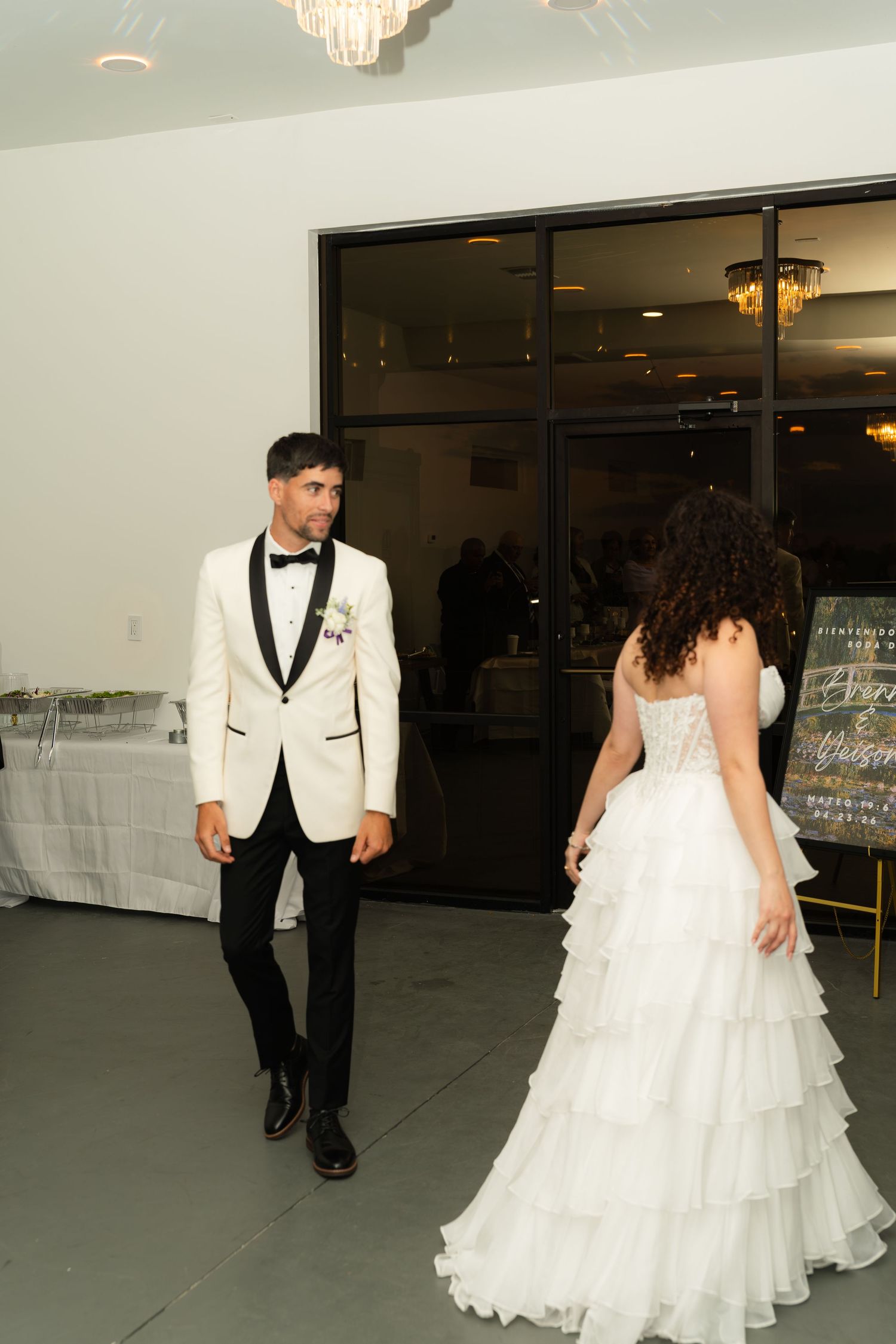 Groom in white tuxedo and bride in tiered white gown making grand entrance at wedding reception.