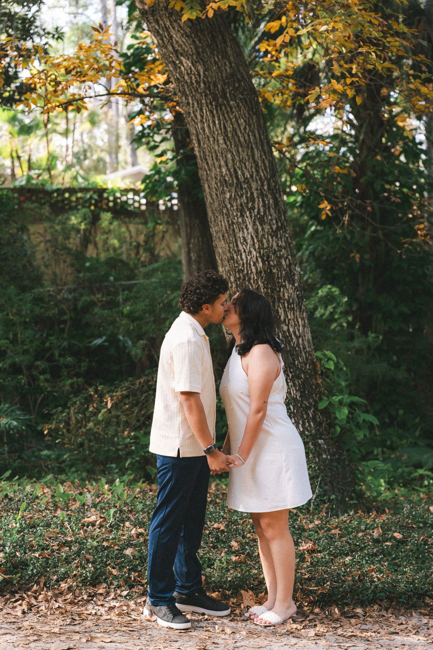 A couple shares a tender moment together under autumn trees in a woodland setting.
