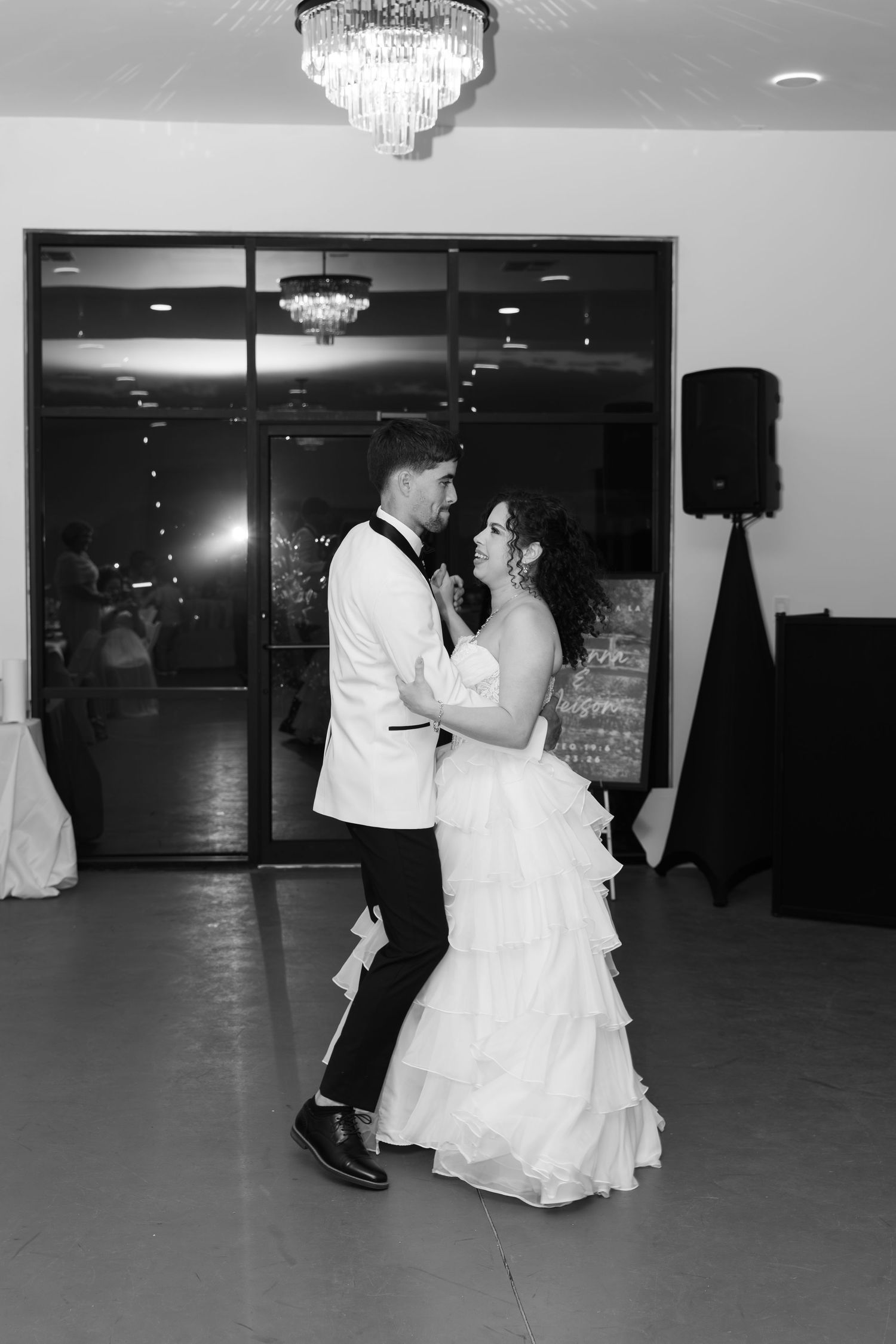 Bride and groom share their first dance under a crystal chandelier in black and white wedding reception photo.