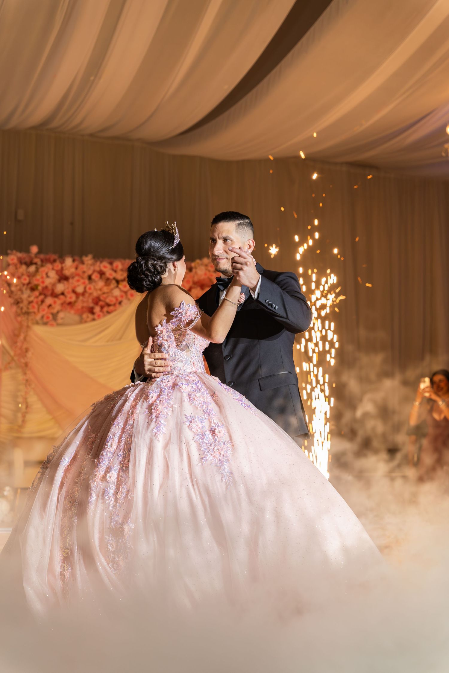 A couple shares their first dance at a wedding reception, surrounded by sparkling fireworks and romantic fog effects.