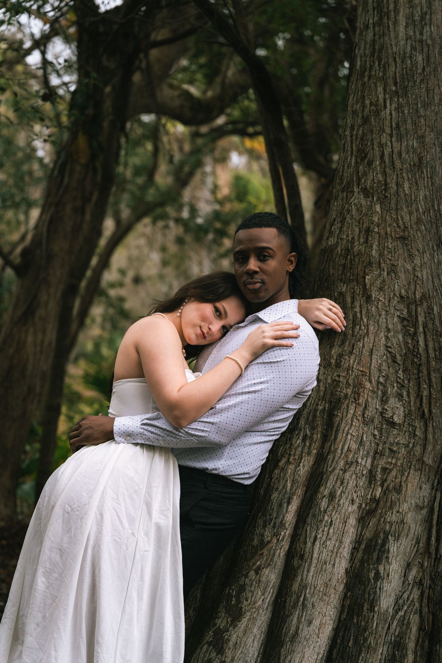 A couple shares intimate moments in a romantic outdoor photoshoot among trees in a natural setting.