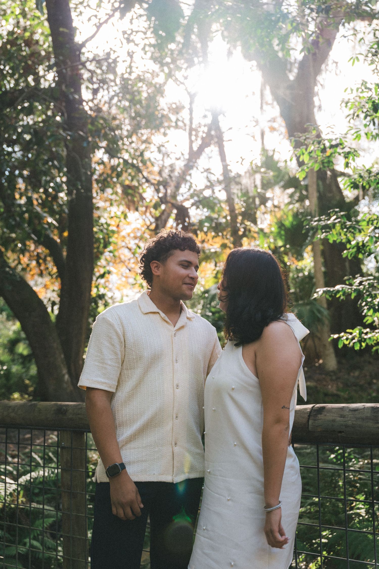 A couple shares a tender moment together in a sunlit garden setting with lush greenery in the background.
