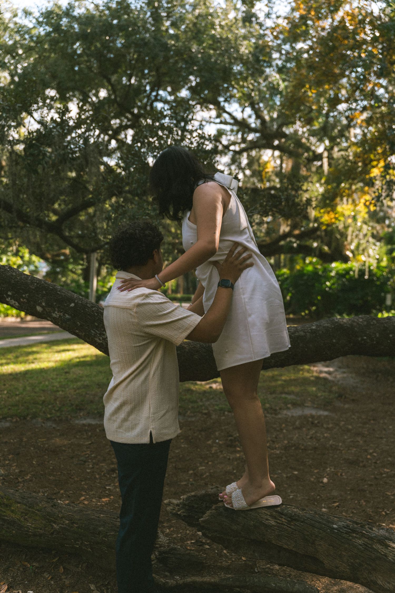 Two people practice martial arts kicks in a park setting with trees and sunlight filtering through the branches.