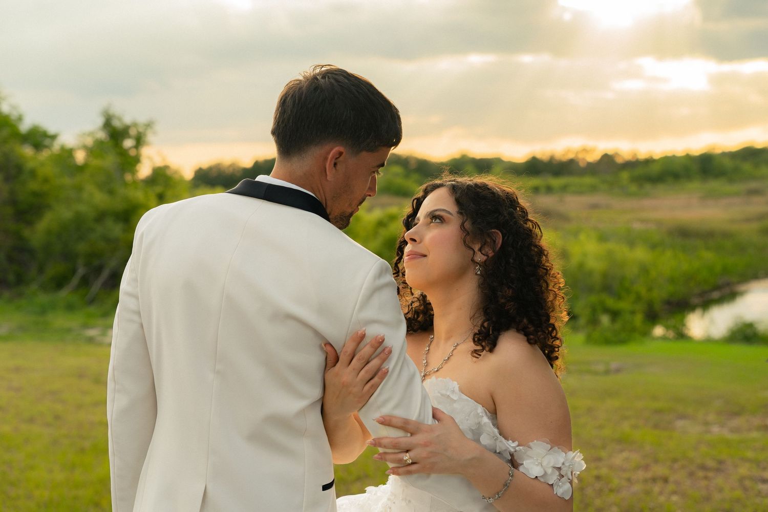 Newlywed couple sharing romantic moment at sunset in lush green outdoor wedding venue.