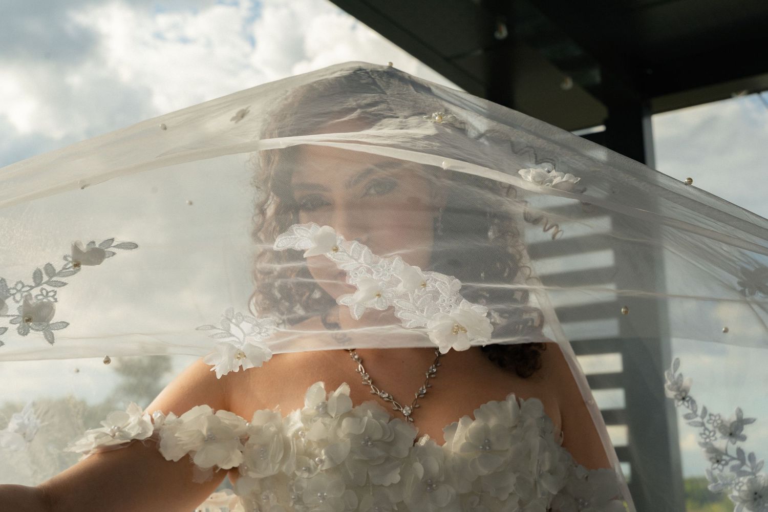 Beautiful bride partially veiled in lace wedding veil wearing floral strapless gown.
