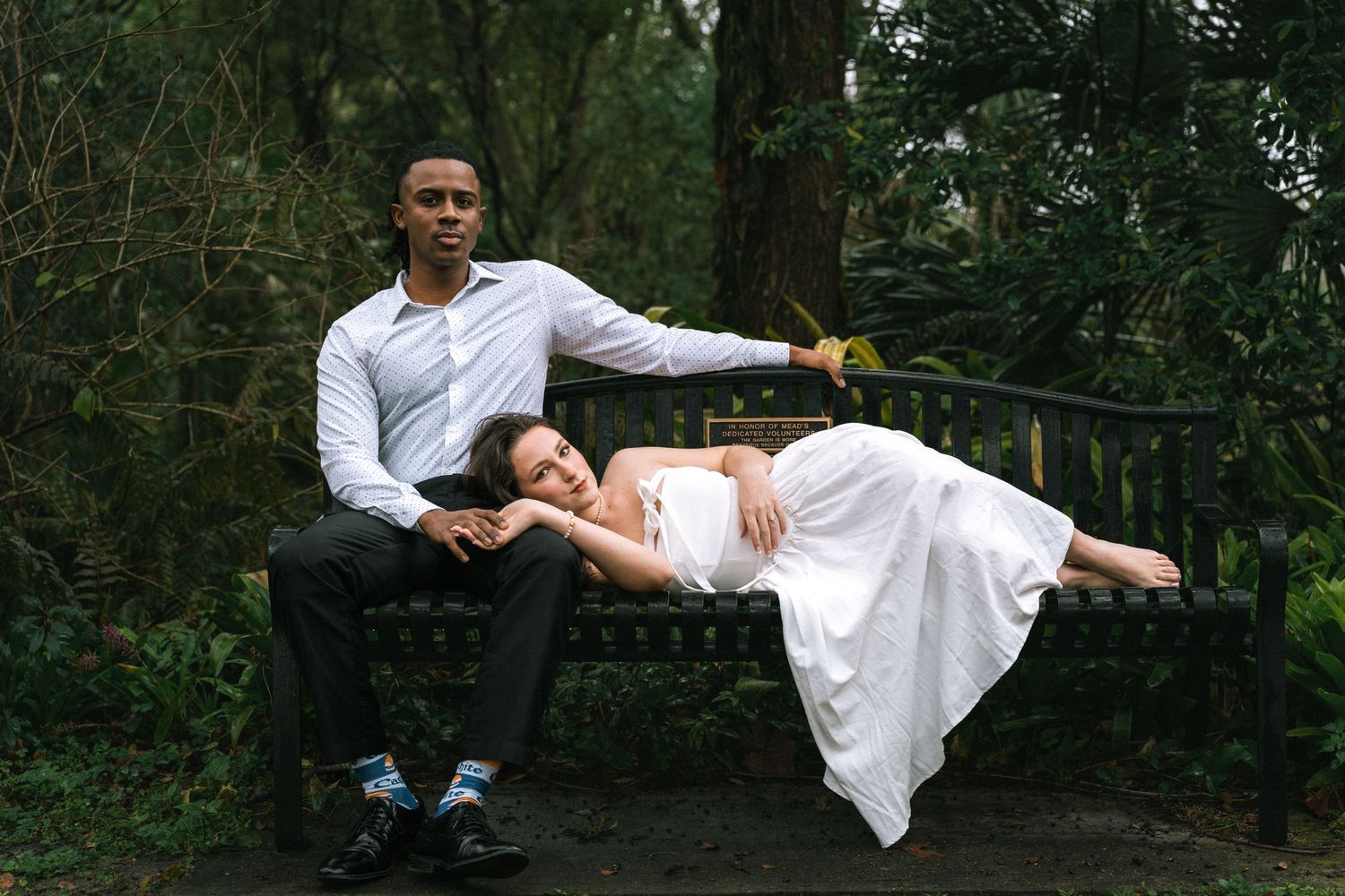 A couple in wedding attire poses together in a lush green garden setting for romantic photos.