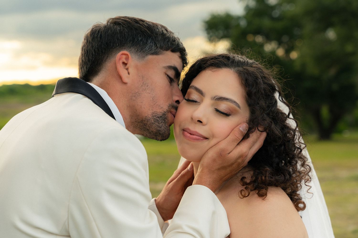 Groom kissing bride on cheek at sunset during romantic outdoor wedding photo session.