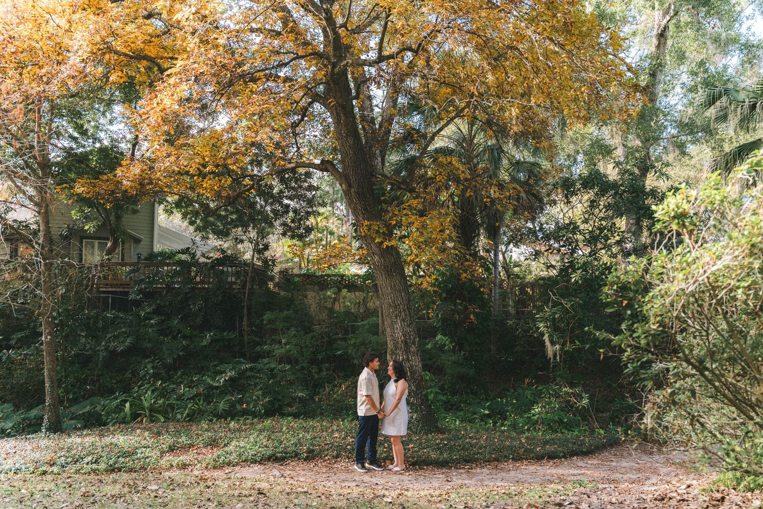 Couple walking through a scenic autumn forest path with golden leaves and tall trees.