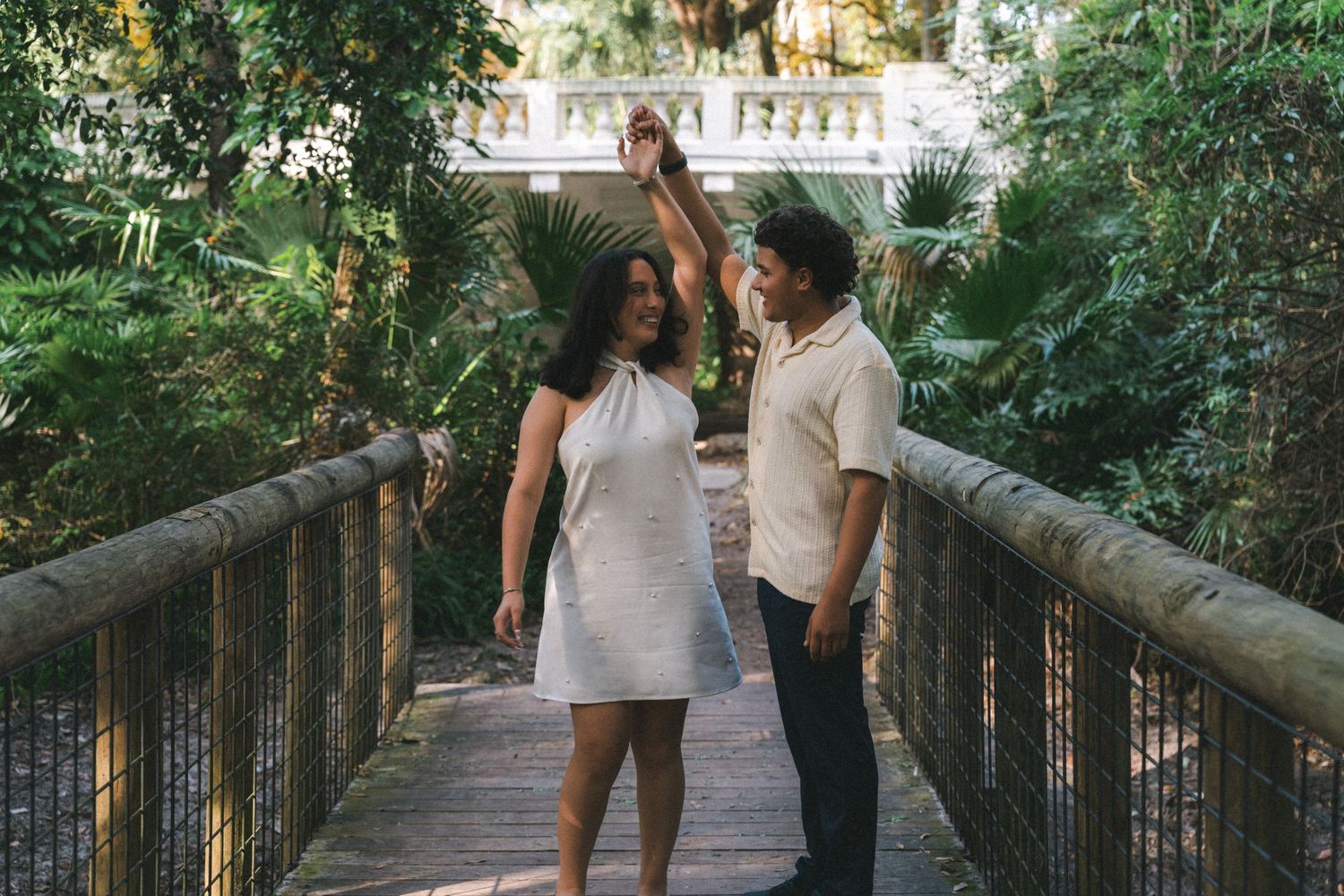 A couple walks together on a wooden boardwalk path through lush green forest scenery.