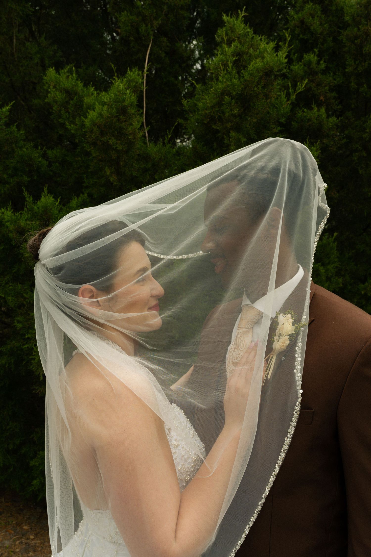 Bride and groom sharing an intimate moment under a flowing white wedding veil outdoors.