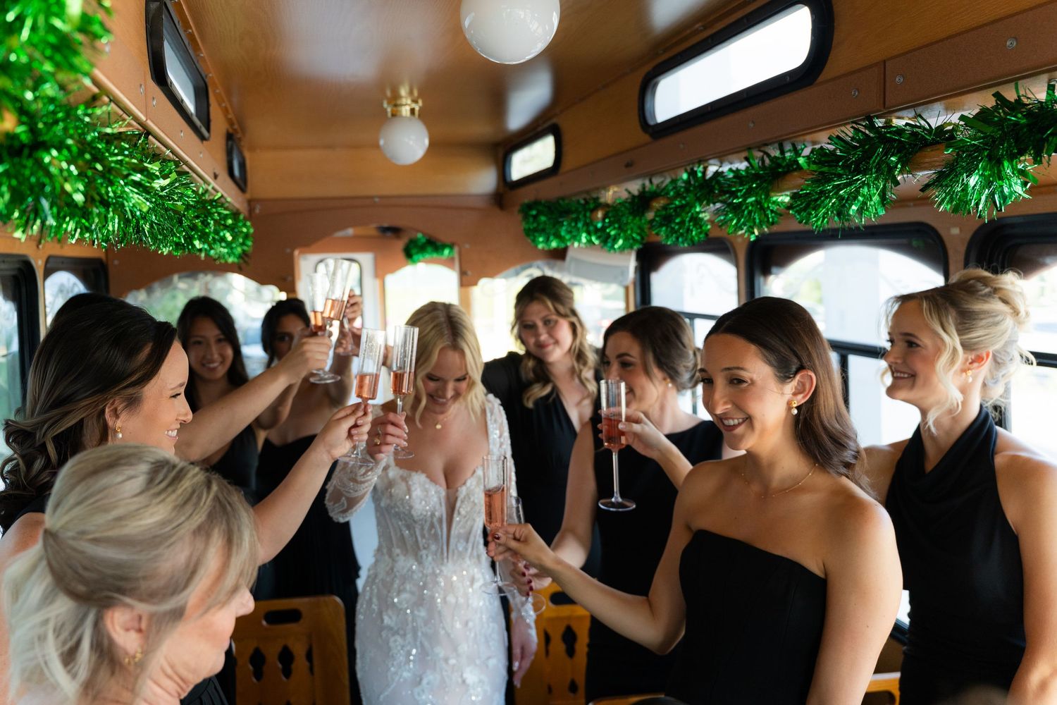 Bride in white gown toasting champagne with bridesmaids in black dresses on decorated party trolley.