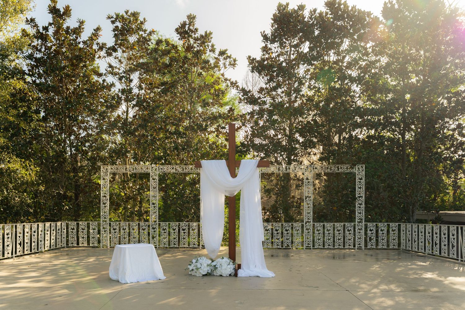 Elegant outdoor wedding ceremony arch draped in white fabric, flanked by decorative panels, surrounded by lush green trees.