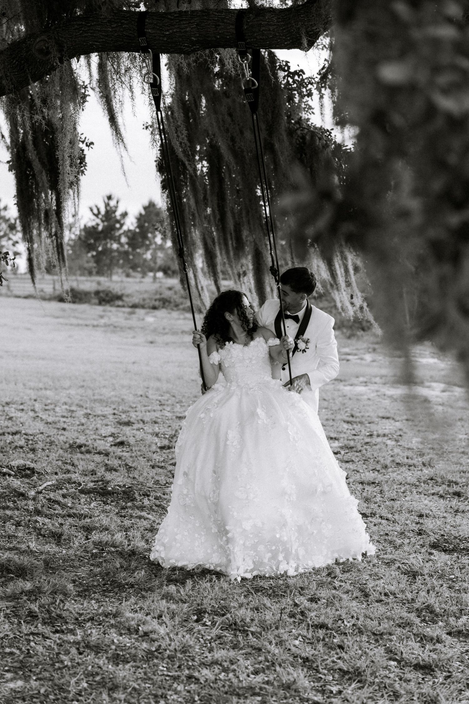 Black and white photo of bride and groom sharing a romantic moment by a rustic tree swing draped with Spanish moss.