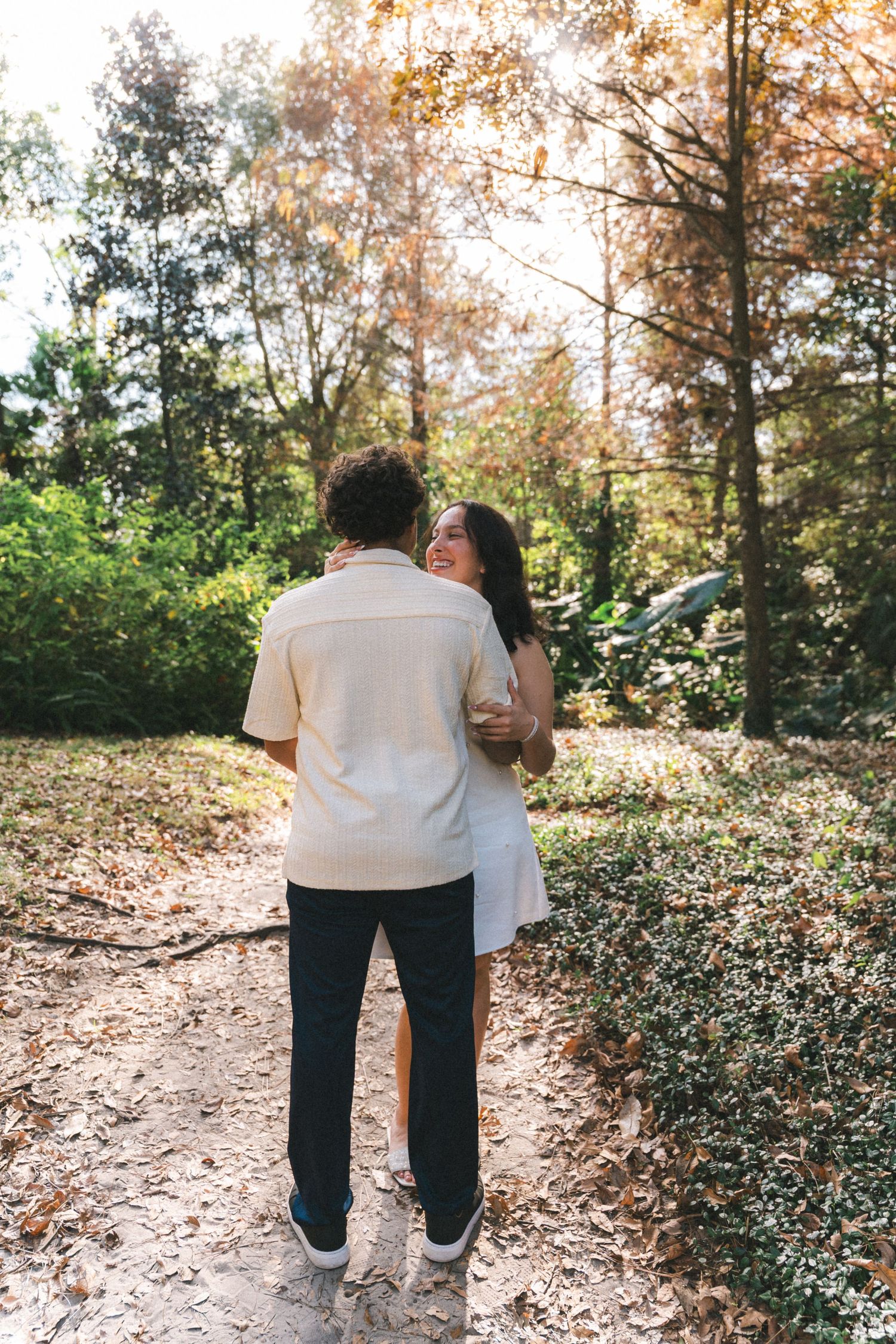 A couple walking together on a leaf-covered path through an autumn forest landscape.