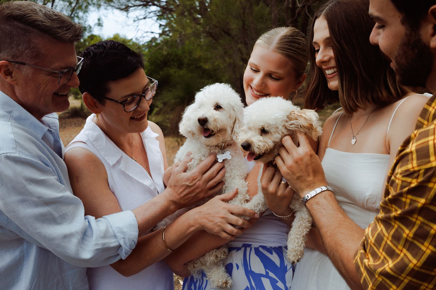 Group of people cuddling and playing with a small white fluffy dog outdoors.