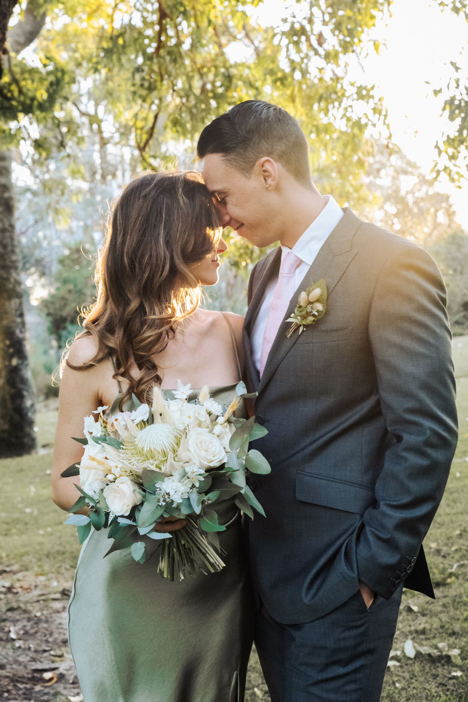 Newlyweds share an intimate moment in a garden setting with white floral bouquet.