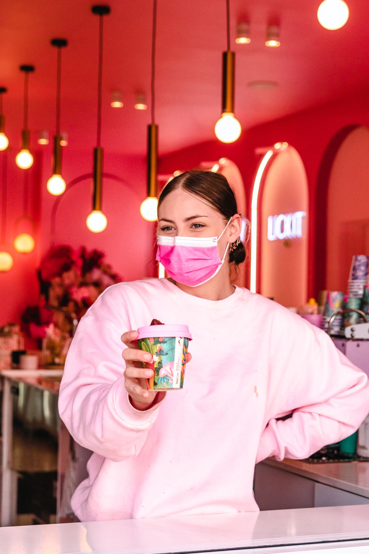 Ice cream service counter illuminated by warm hanging pendant lights in a pink-toned environment.