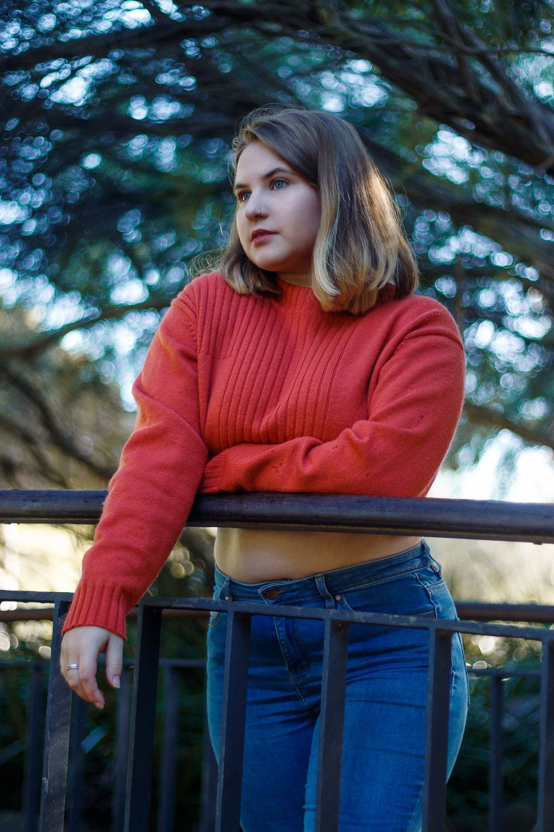 Casual outdoor portrait series in red sweater and jeans on balcony.