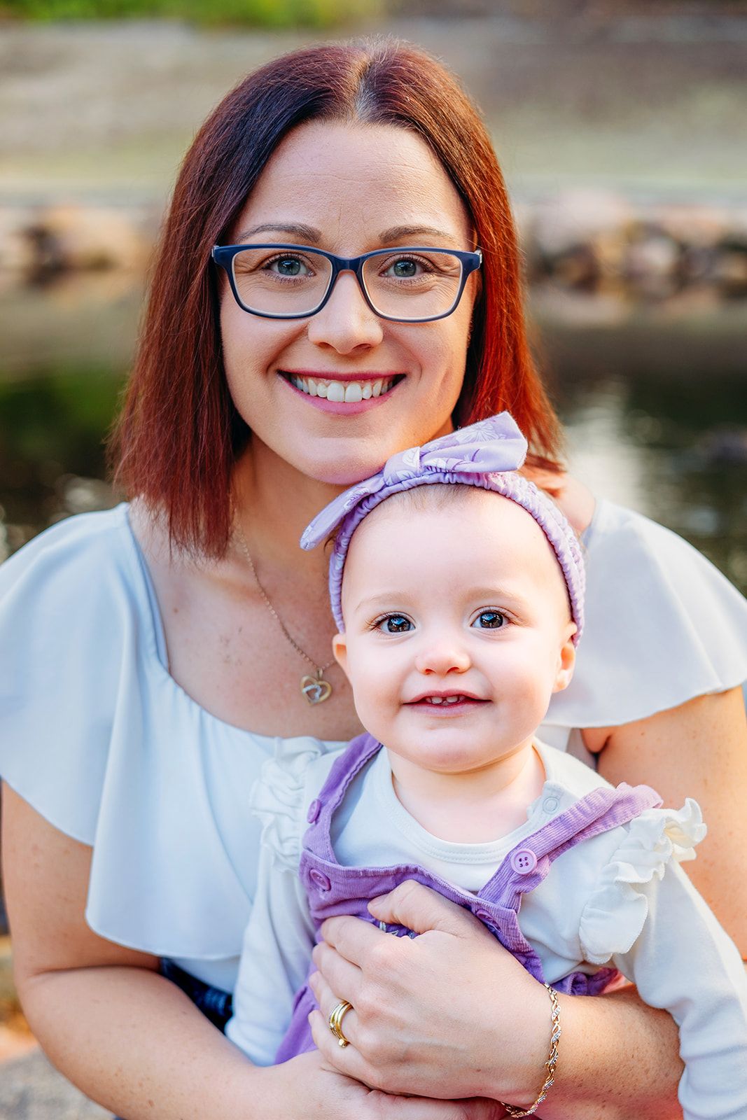 Baby in purple dress being held and smiling during outdoor family photoshoot.