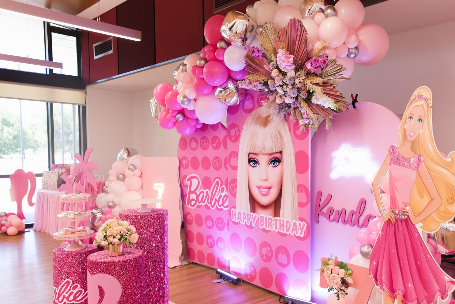 Pink Barbie themed birthday party setup with balloon arch, floral decorations, and personalized backdrop with name Kendra.