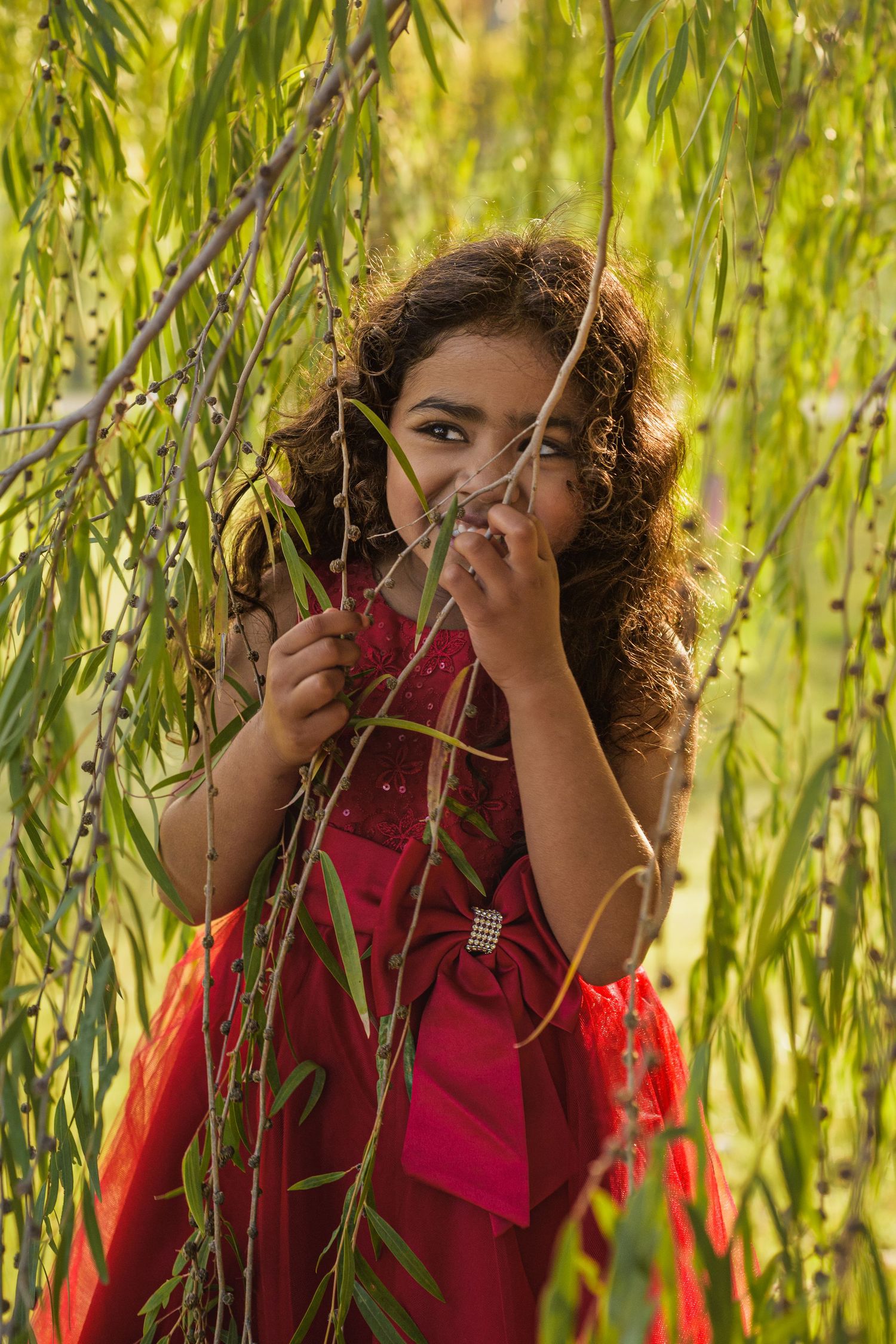 Person peeking through willow tree branches in red clothing.