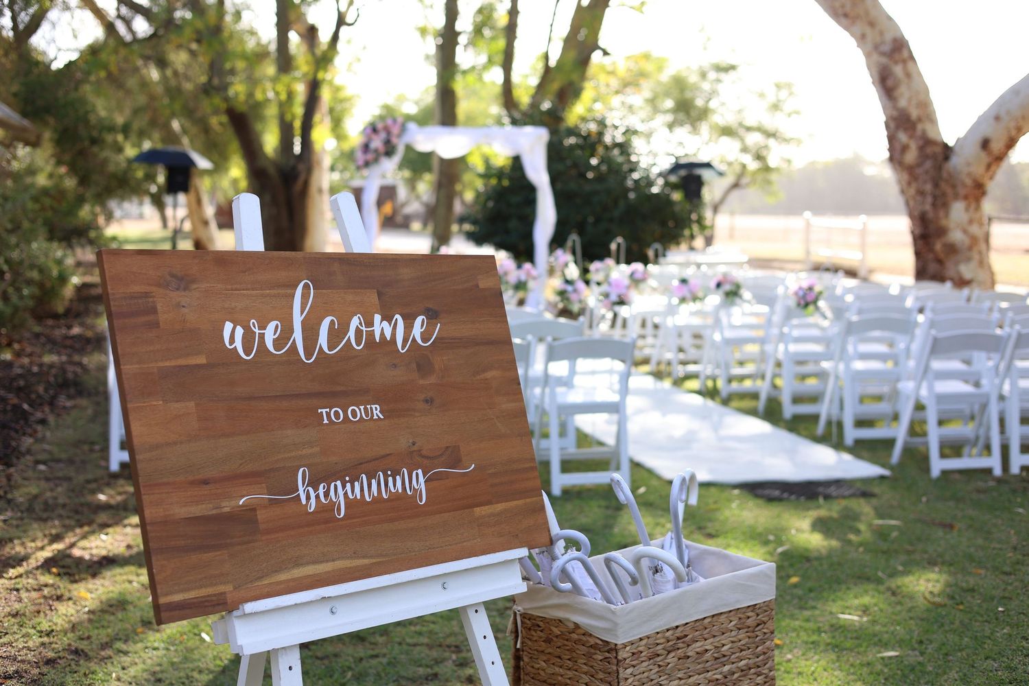 Rustic wooden welcome signs and wedding decor arranged outdoors with white chairs in the background.