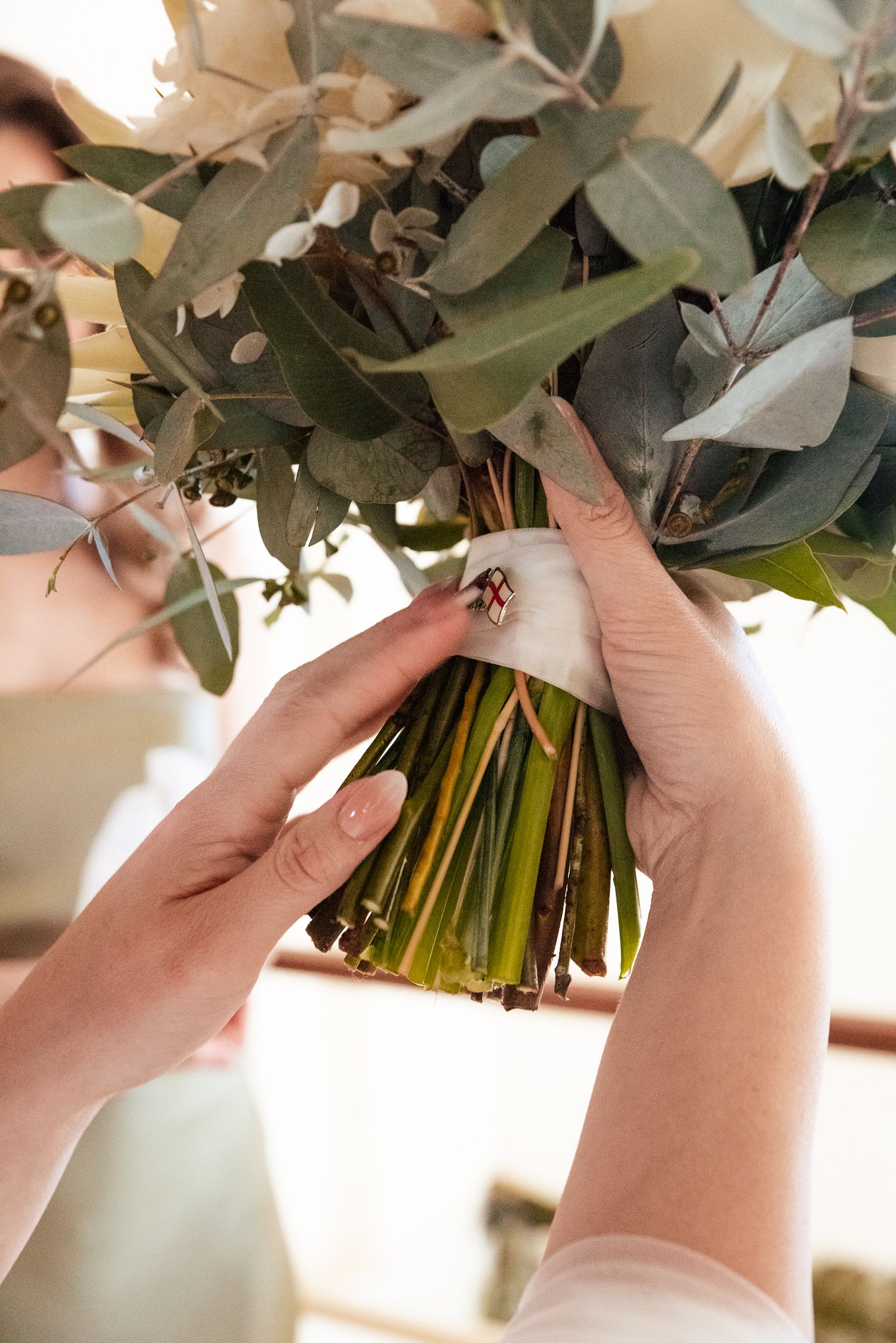 Close-up of hands arranging white and green wedding bouquet with eucalyptus leaves.