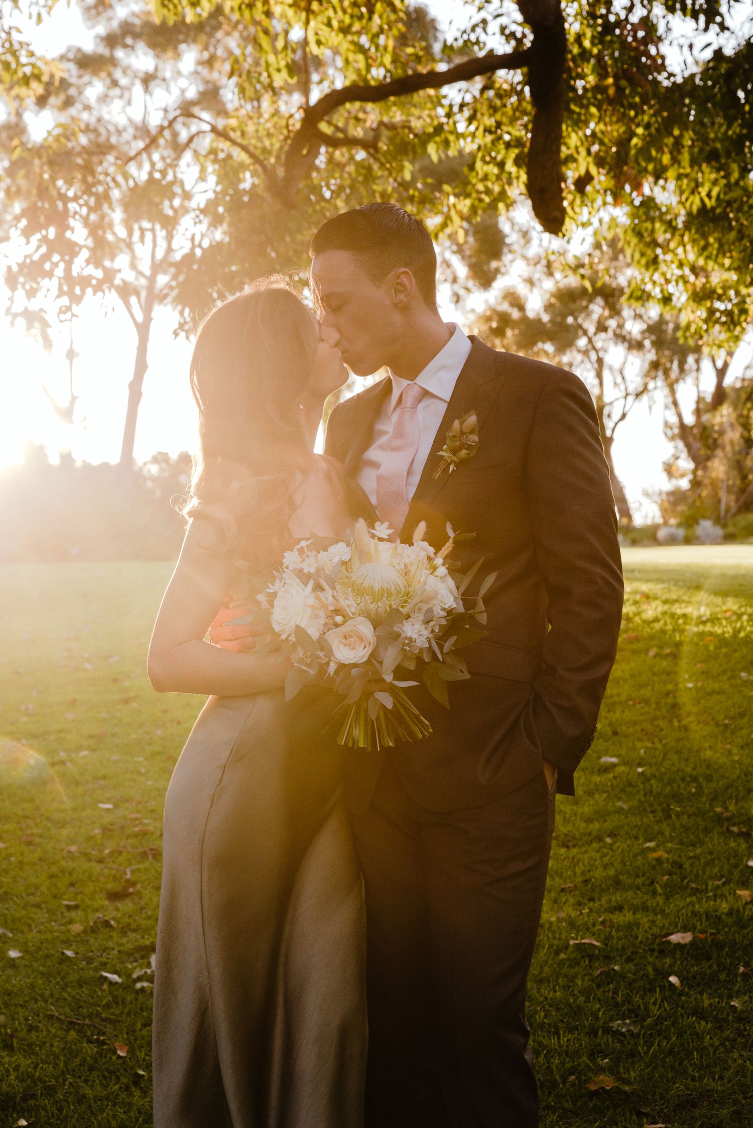 Silhouettes of a wedding couple embracing in golden sunset light with trees in the background.