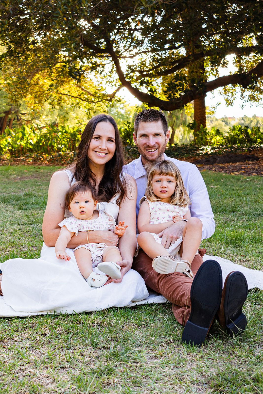 Family relaxes together on grass during golden hour outdoor photoshoot.