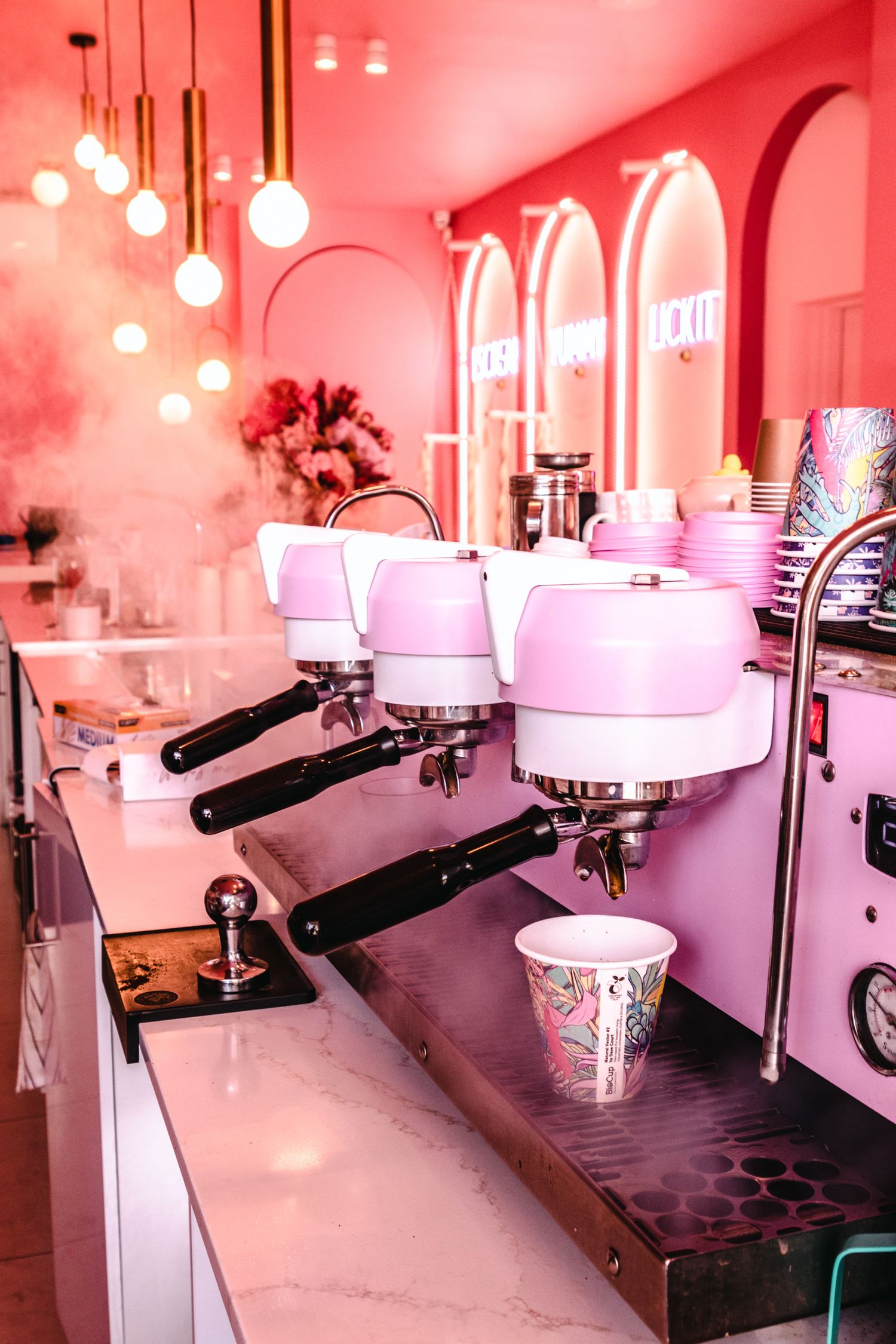 Modern ice cream parlor interior with hanging lights and marble countertops bathed in pink lighting.