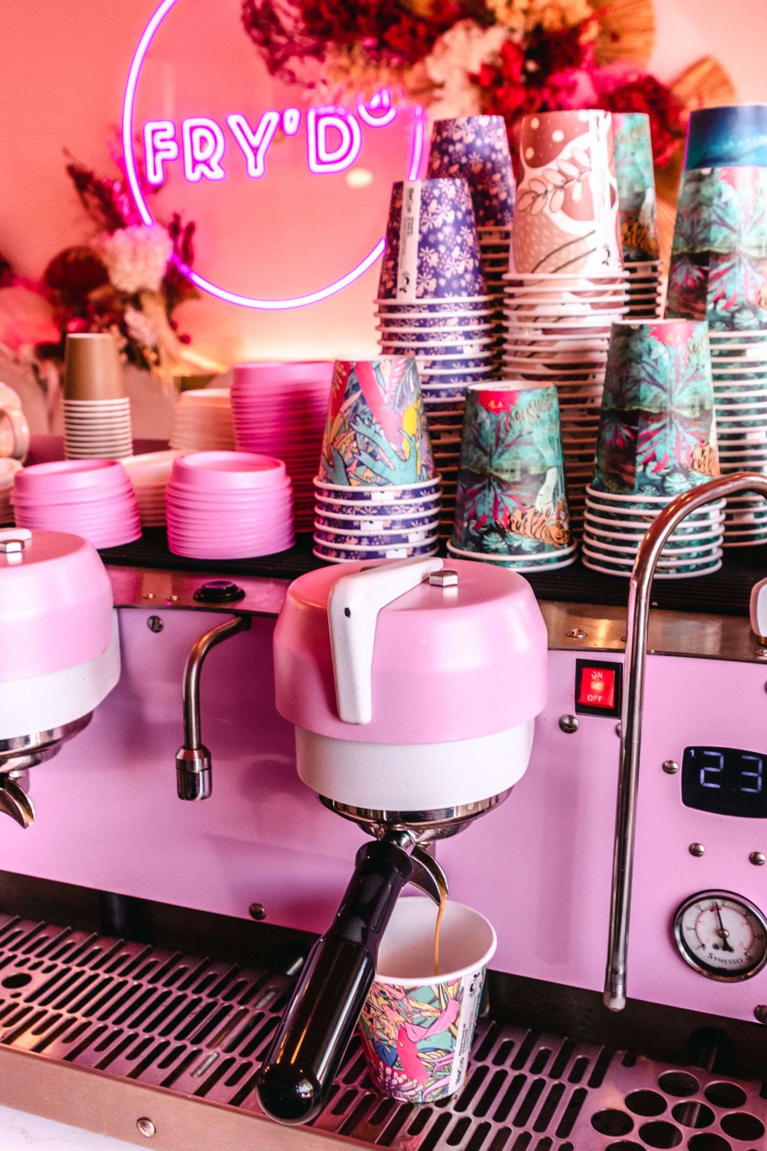 Row of vintage-style ice cream machines with floral patterned cups in pink lighting.