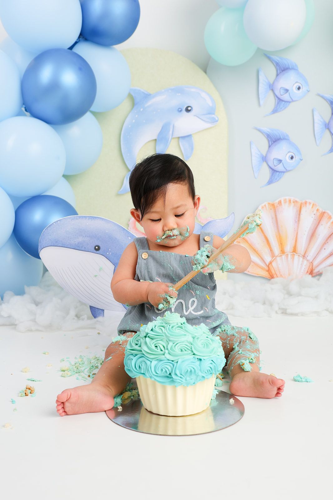 Baby having cake smash photo session with turquoise frosted cake and ocean themed decorations.