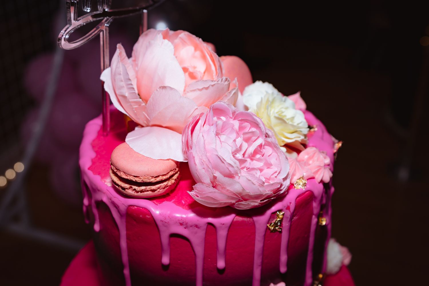 Close-up of pink frosted cake with elegant floral decorations in dramatic lighting.