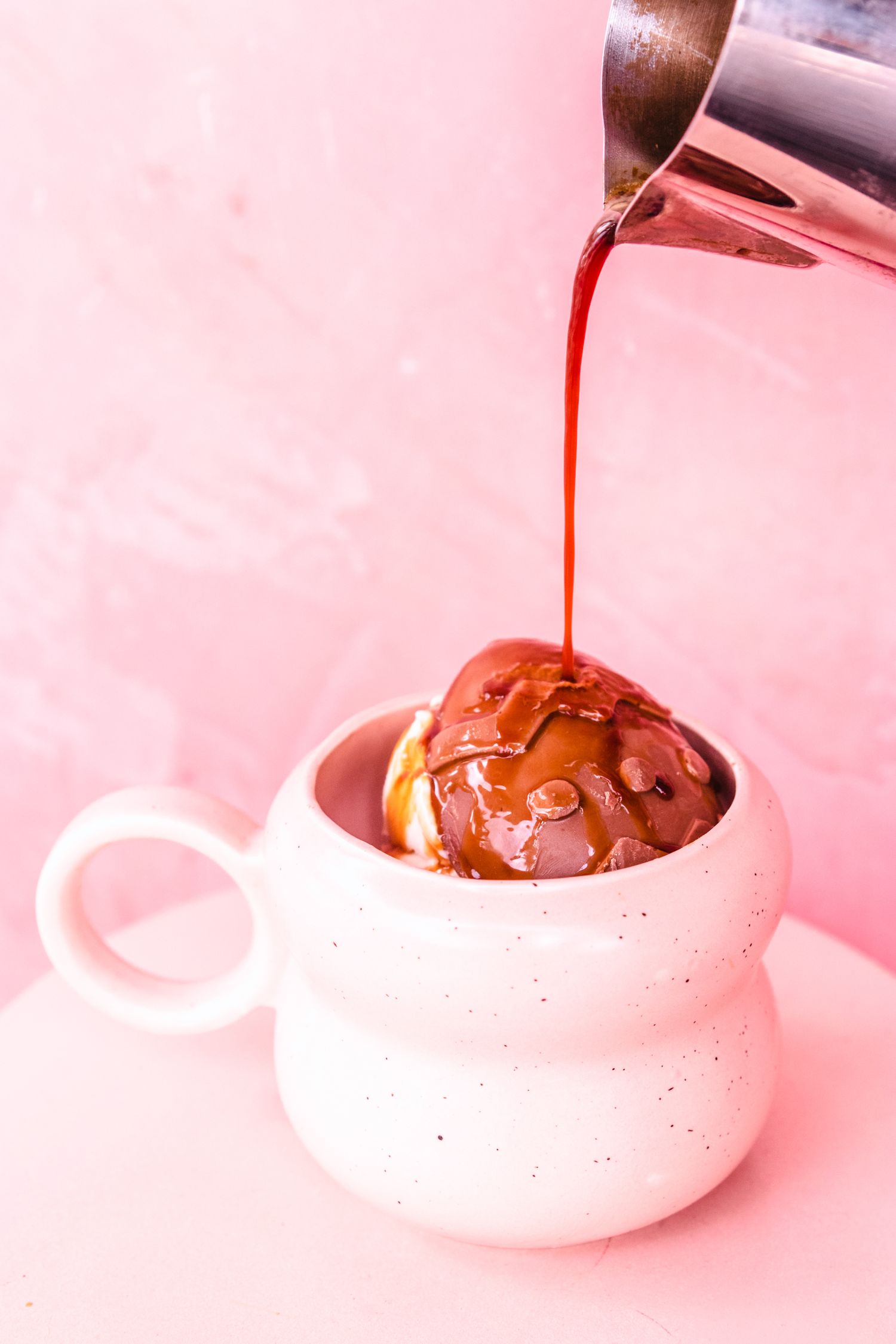 Melted chocolate being poured into white ceramic bowls against a pink background.
