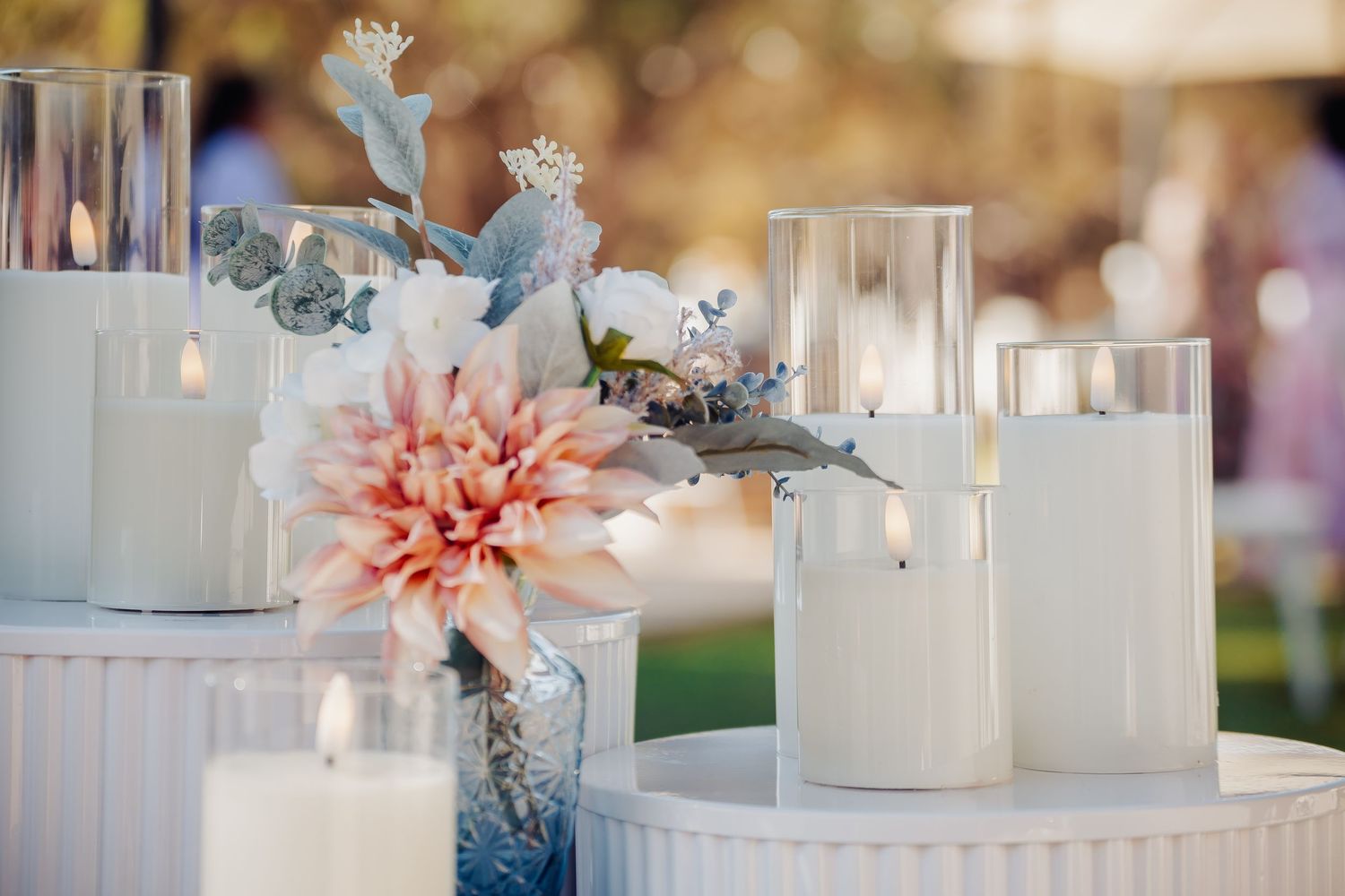 Elegant wedding table decor with white pillar candles in glass holders and a pink dahlia floral arrangement.
