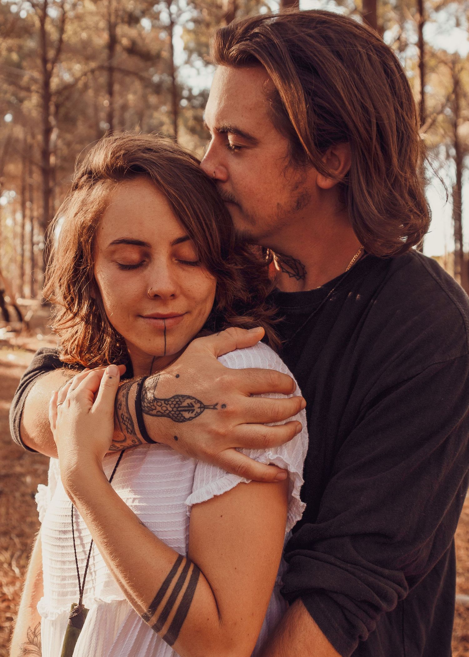 Couple sharing tender moments in warm sunlight among autumn forest trees.