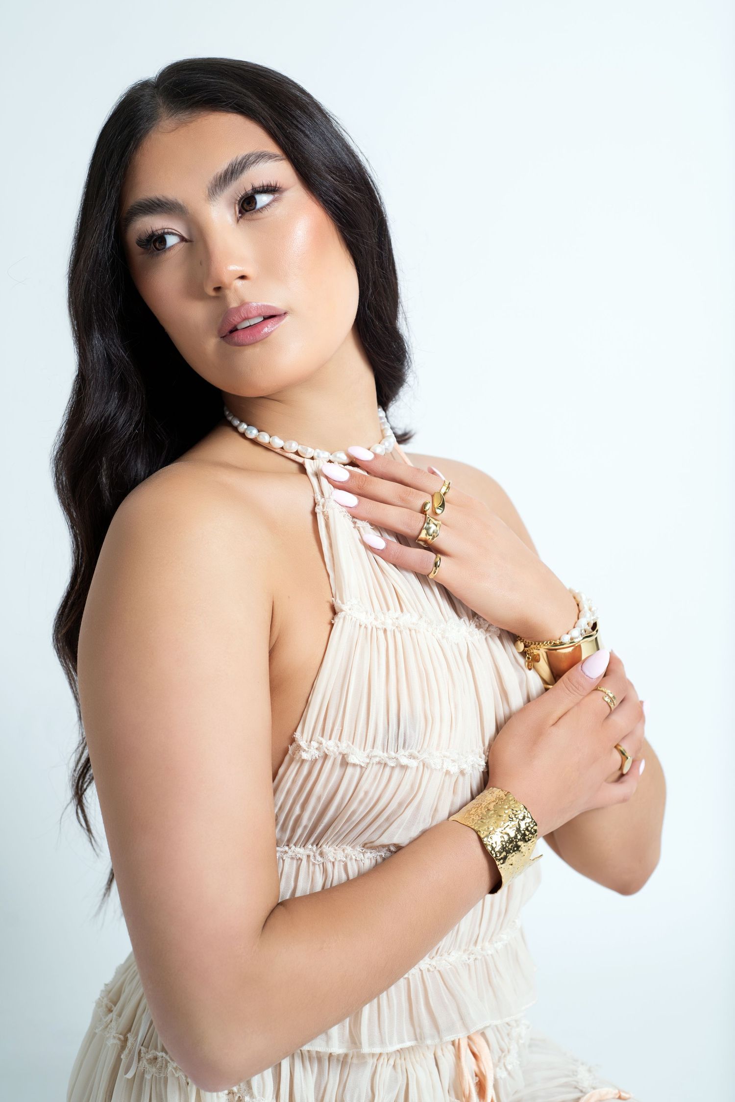Model in cream colored dress posing against white background with jewelry.