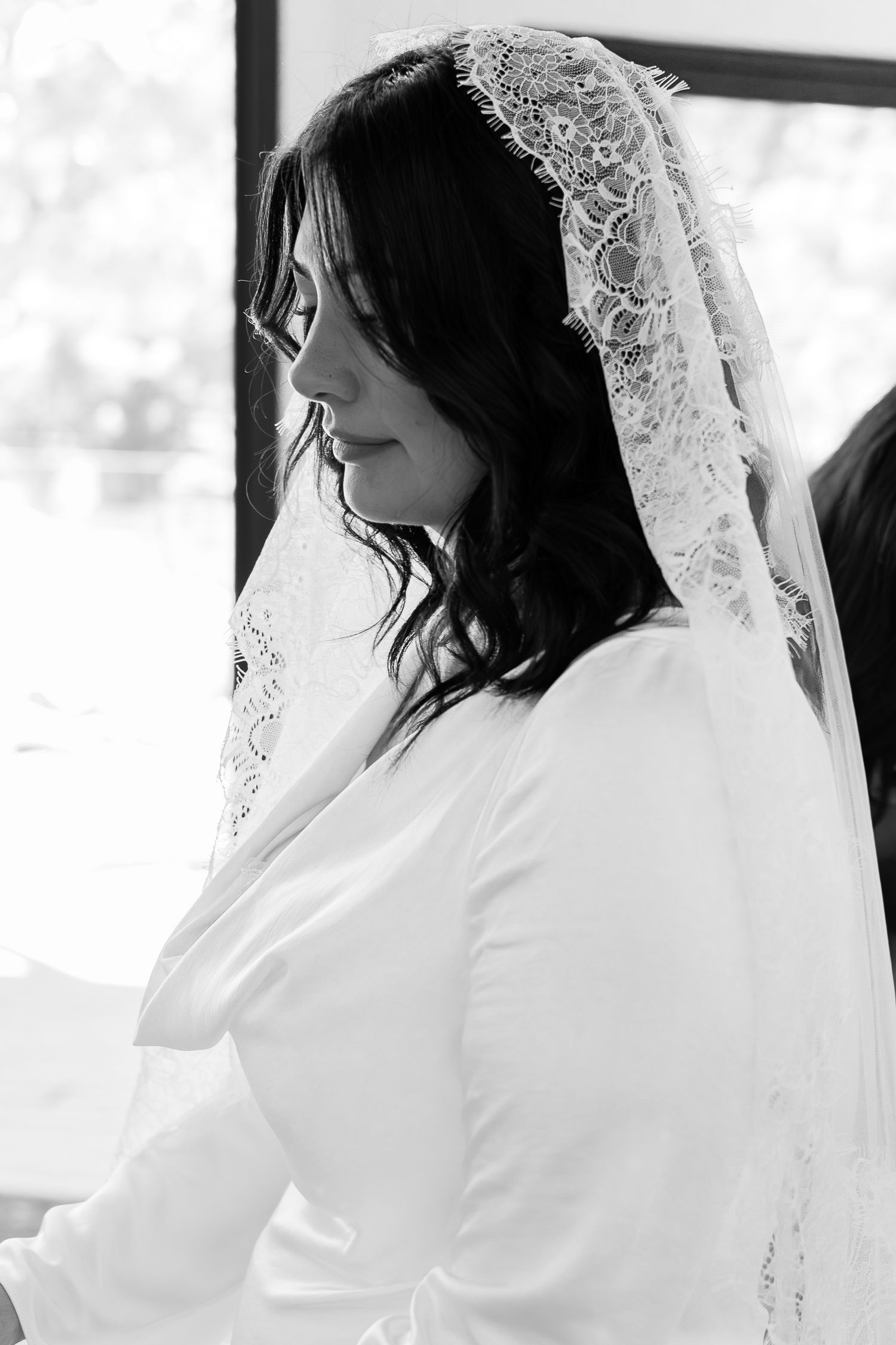 Black and white photo of a bride in a white dress and lace veil, looking down with a serene expression.