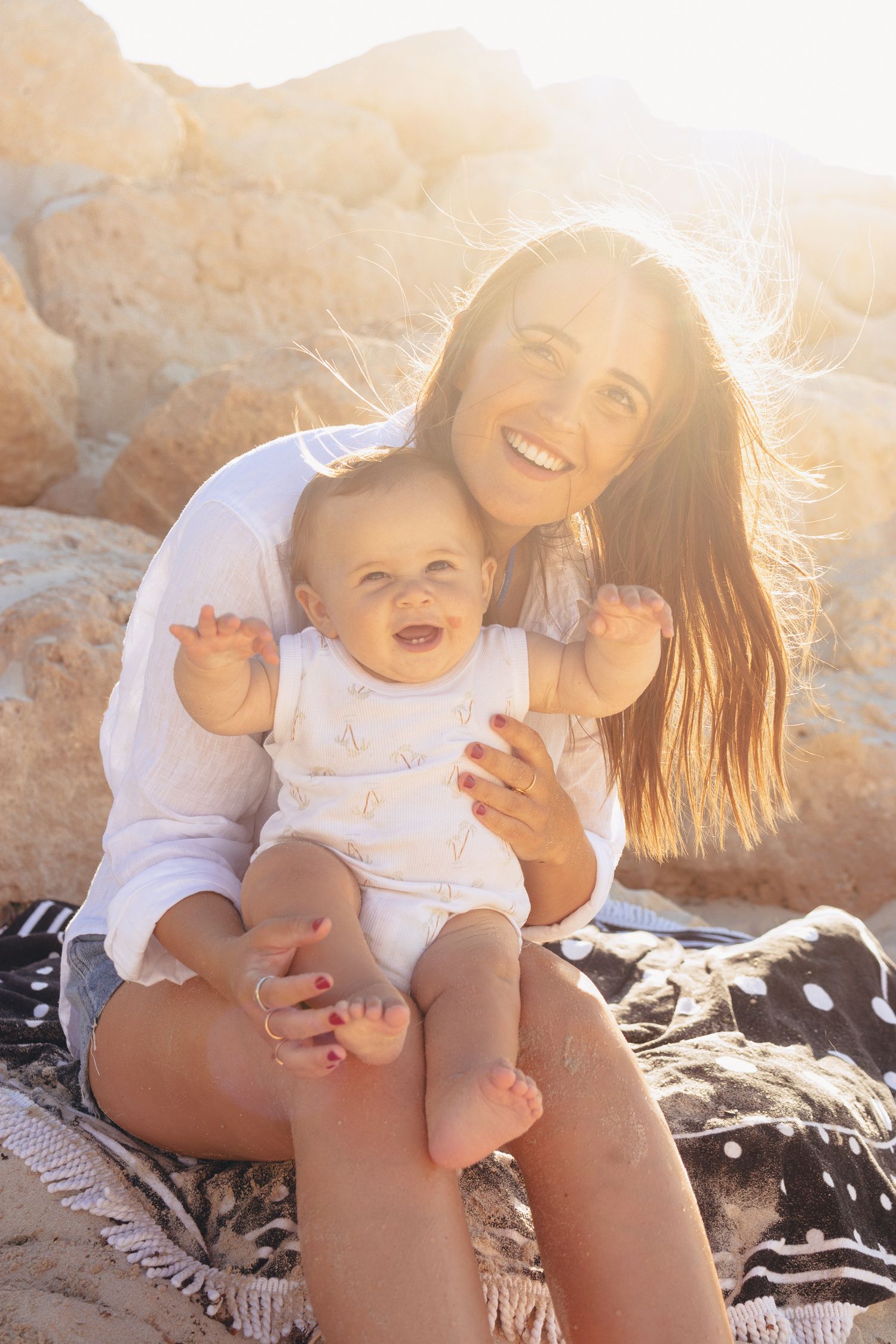 Joyful moment captured between parent and child sitting on blanket at beach during golden hour.