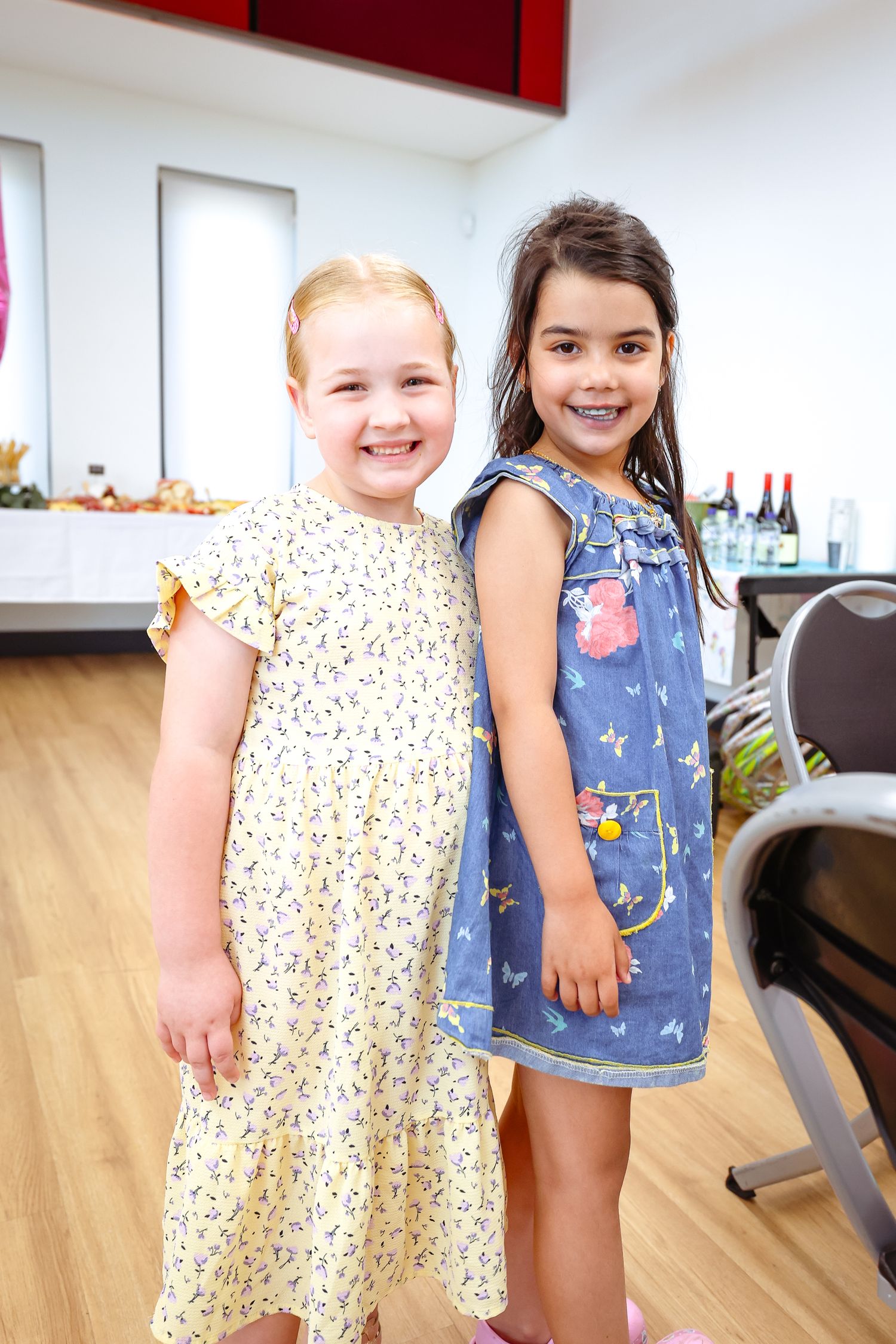 Young children in summer dresses stand together on a light wooden floor.