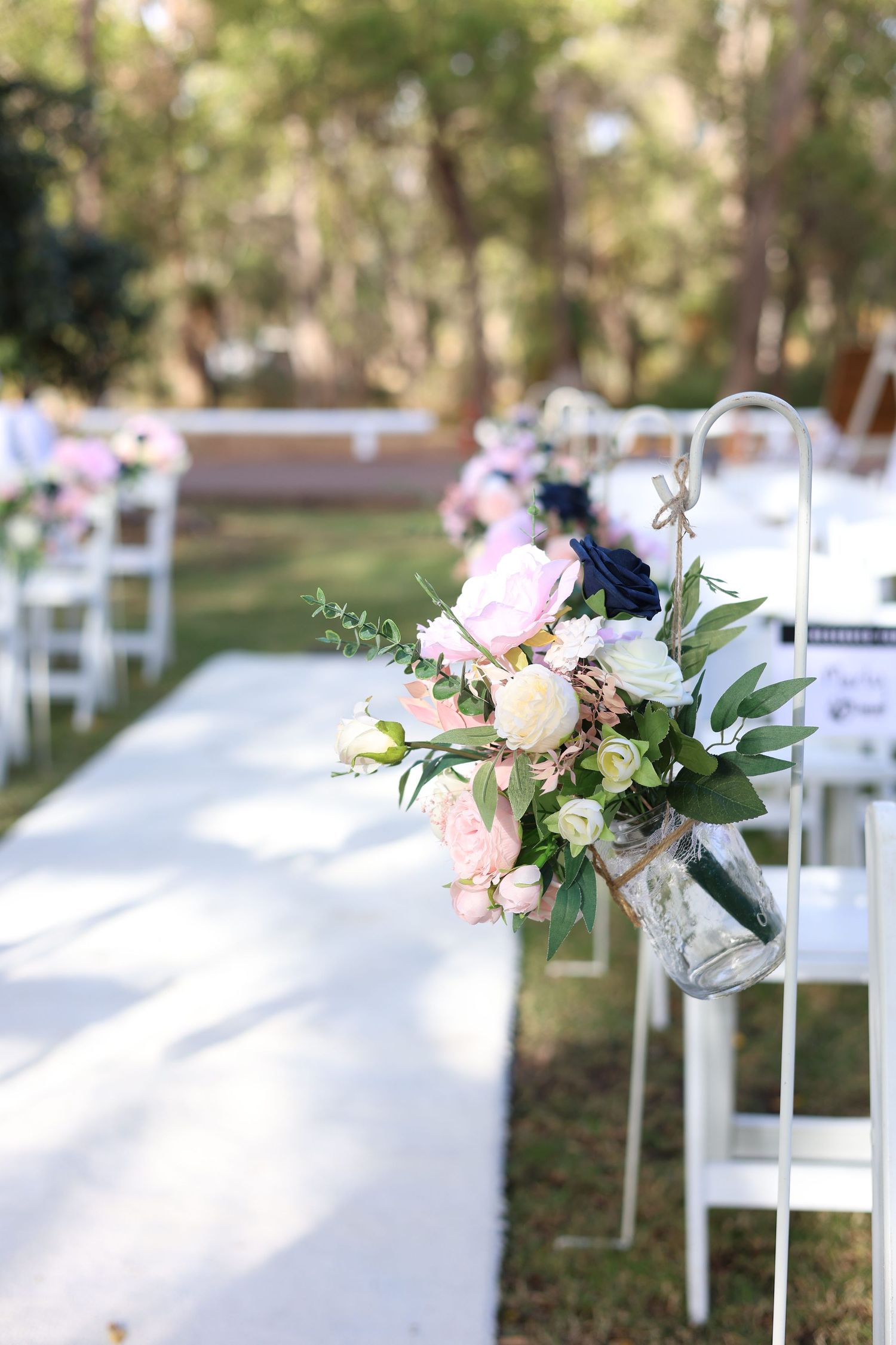Elegant white chairs with pink and white flower arrangements set up for an outdoor garden wedding.