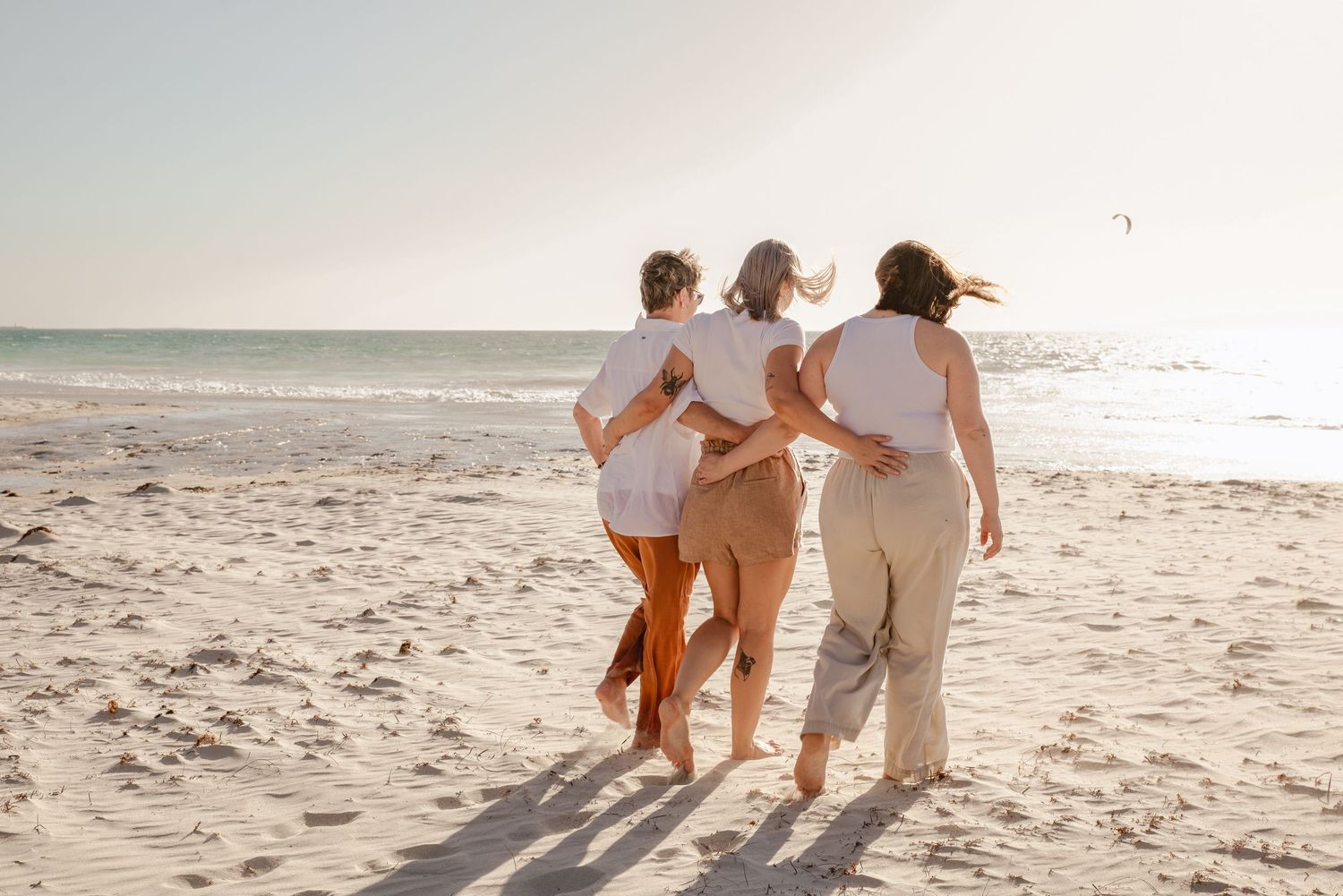 People walking together on a sandy beach at sunset wearing light colored clothing.