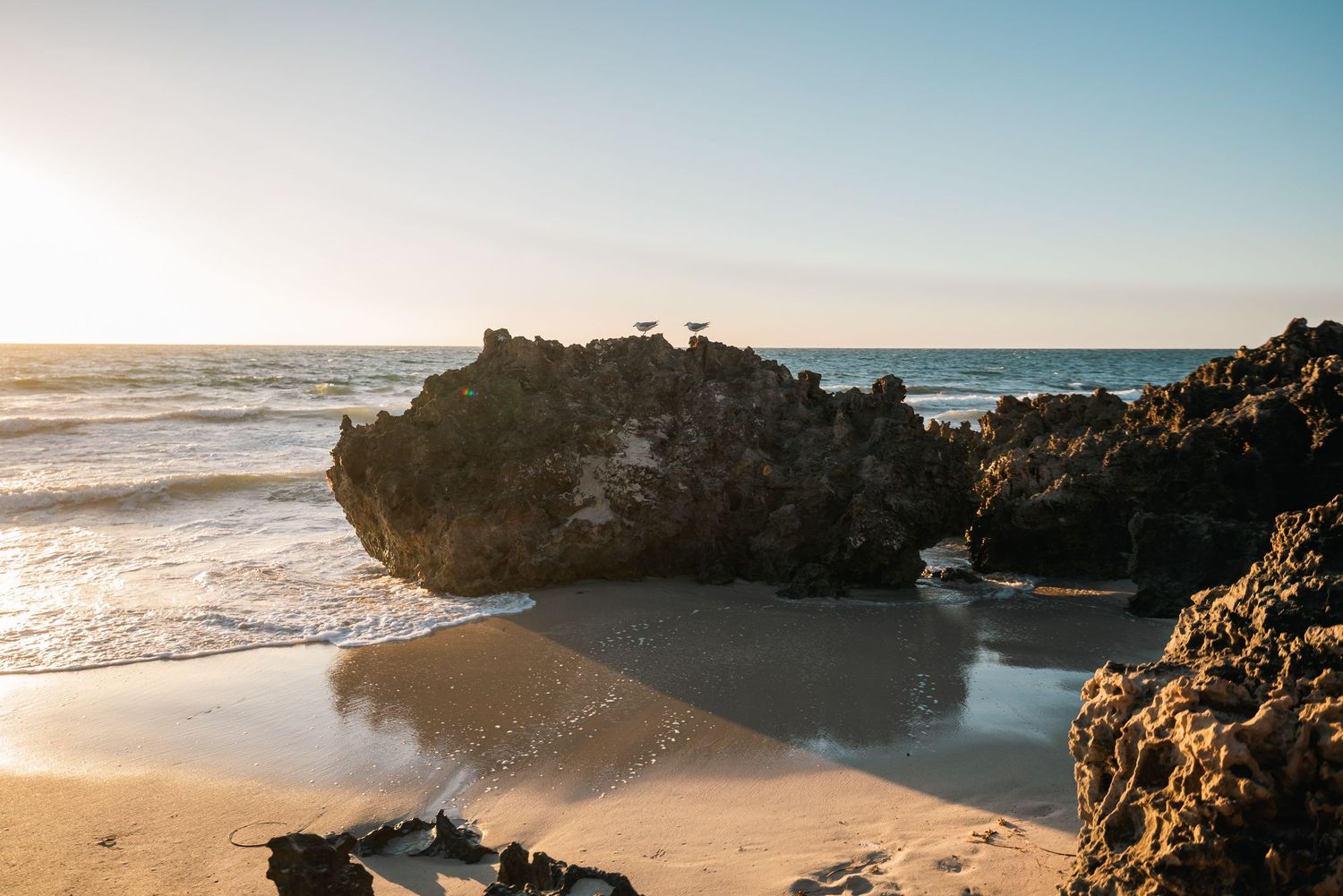 Coastal beach landscape with rocky formations and gentle waves at sunset.
