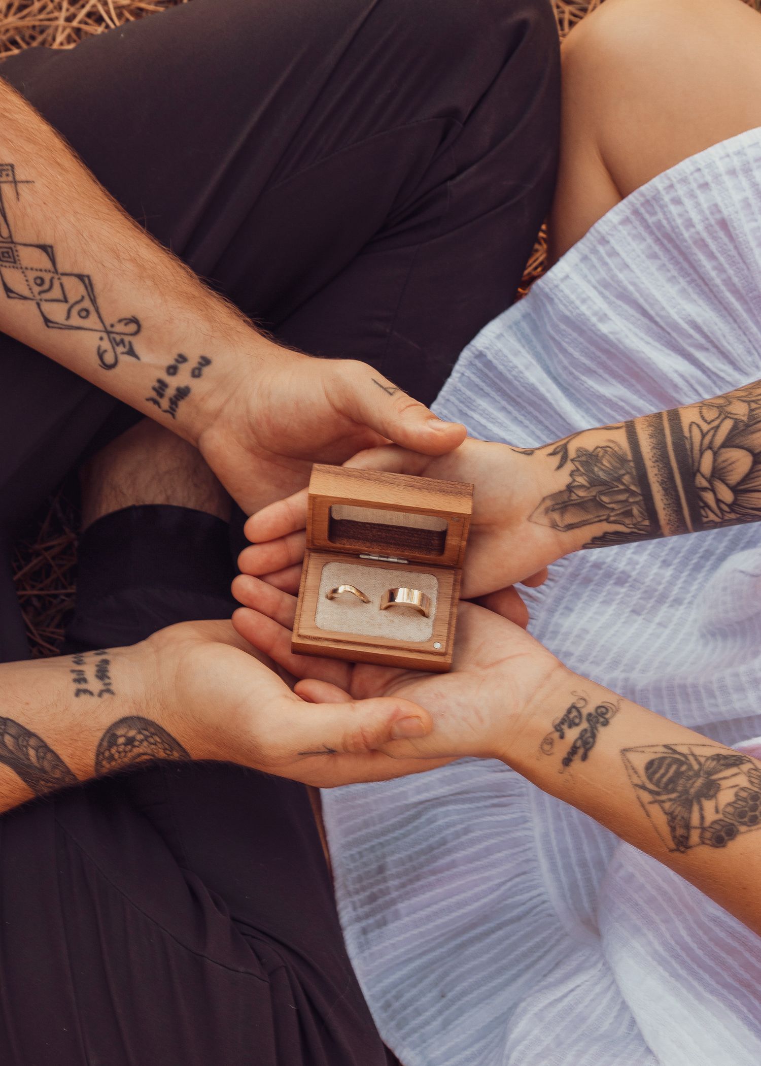 Close-up of tattooed hands exchanging a small wooden box in natural lighting.
