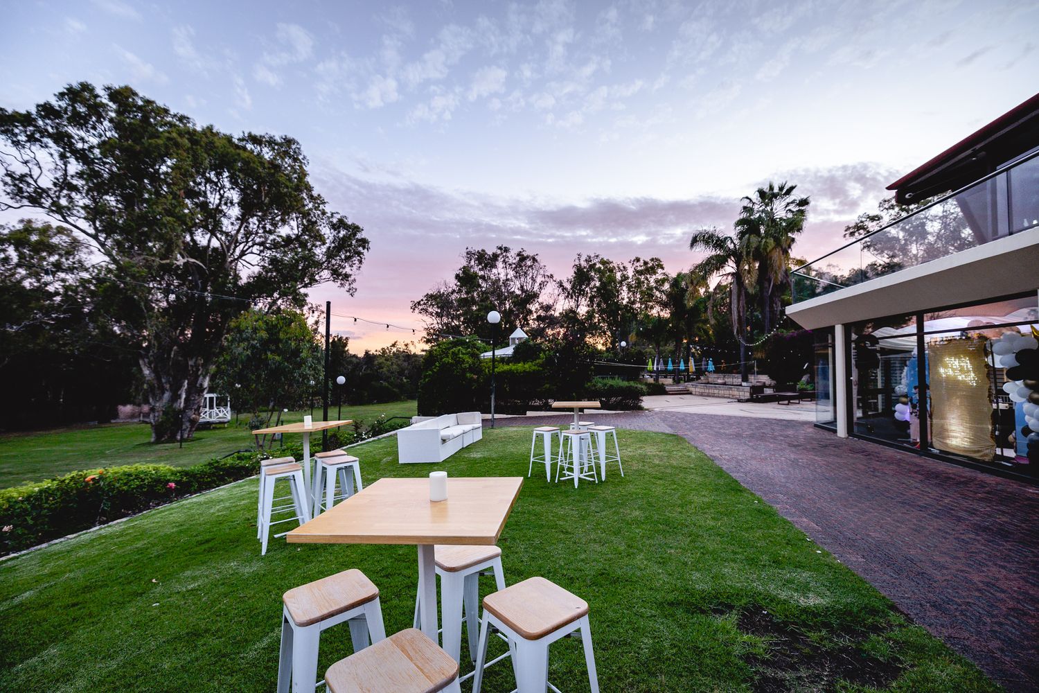 Outdoor venue setup with white furniture on a green lawn at sunset.