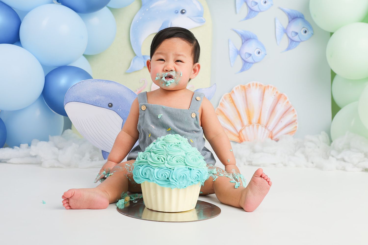 Baby enjoying cake smash session with turquoise frosting and ocean themed decorations.