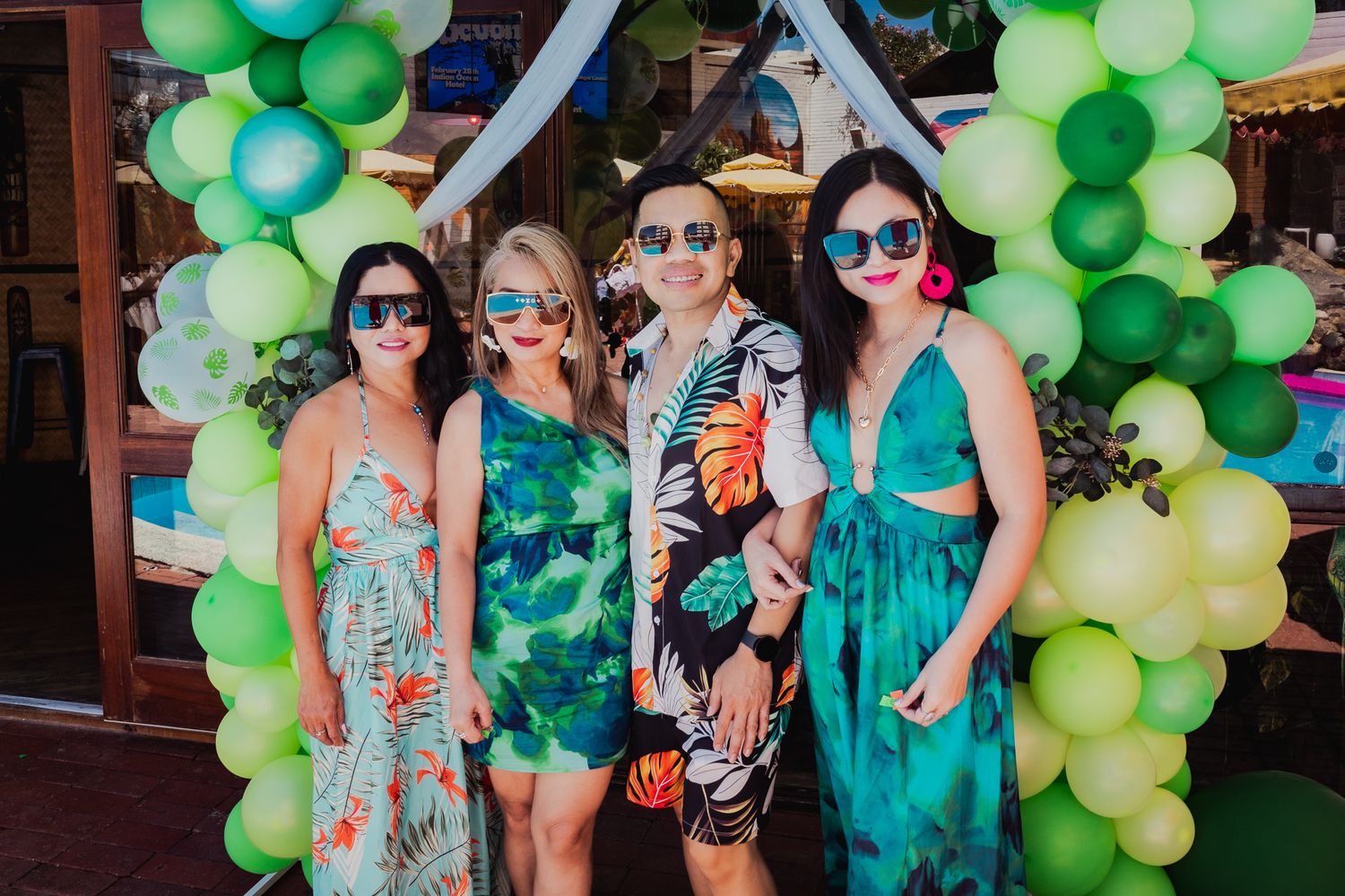 Green balloon arch installation with guests gathered beneath at an outdoor party.