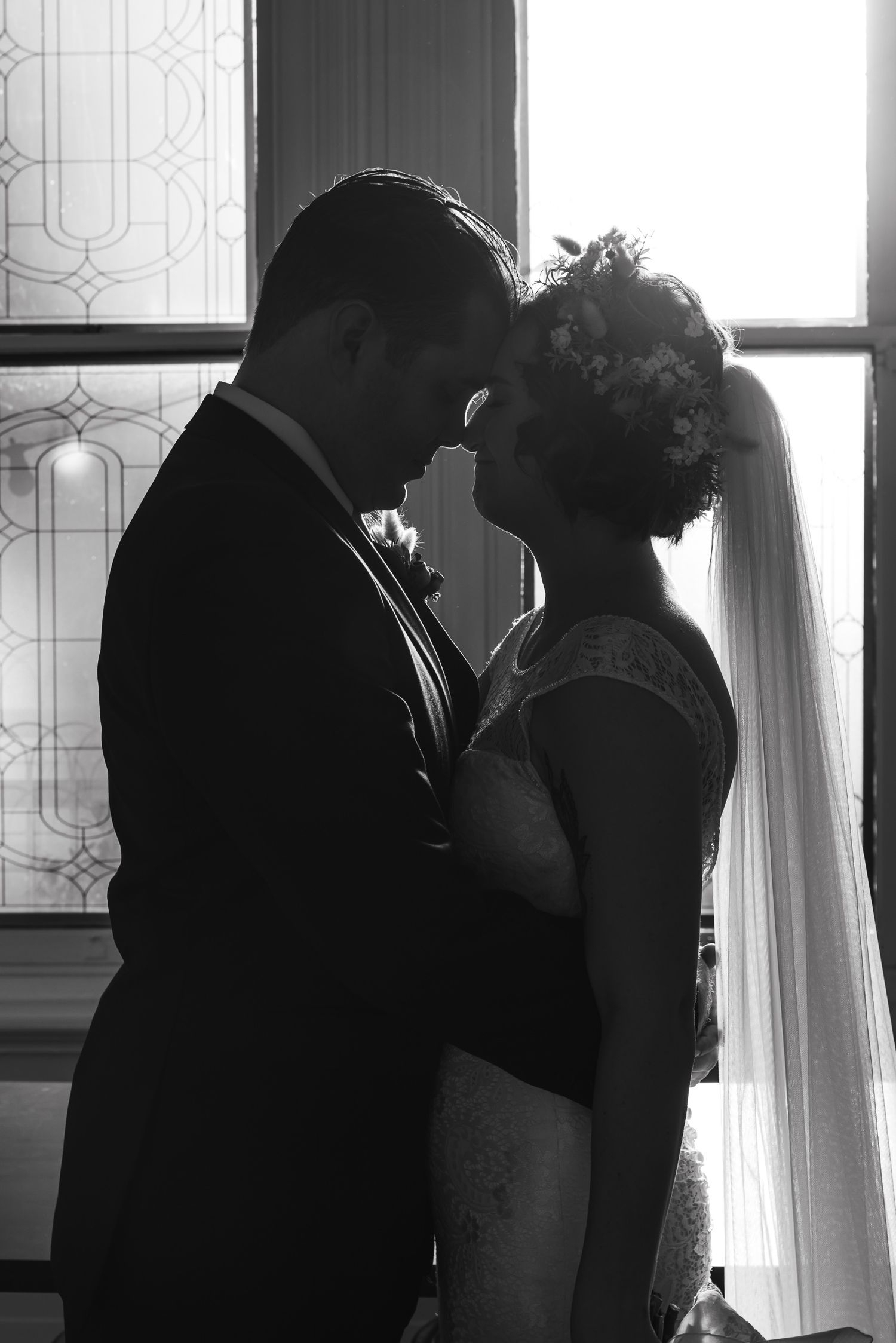 Silhouetted figures in an intimate moment by a window with decorative glass patterns.