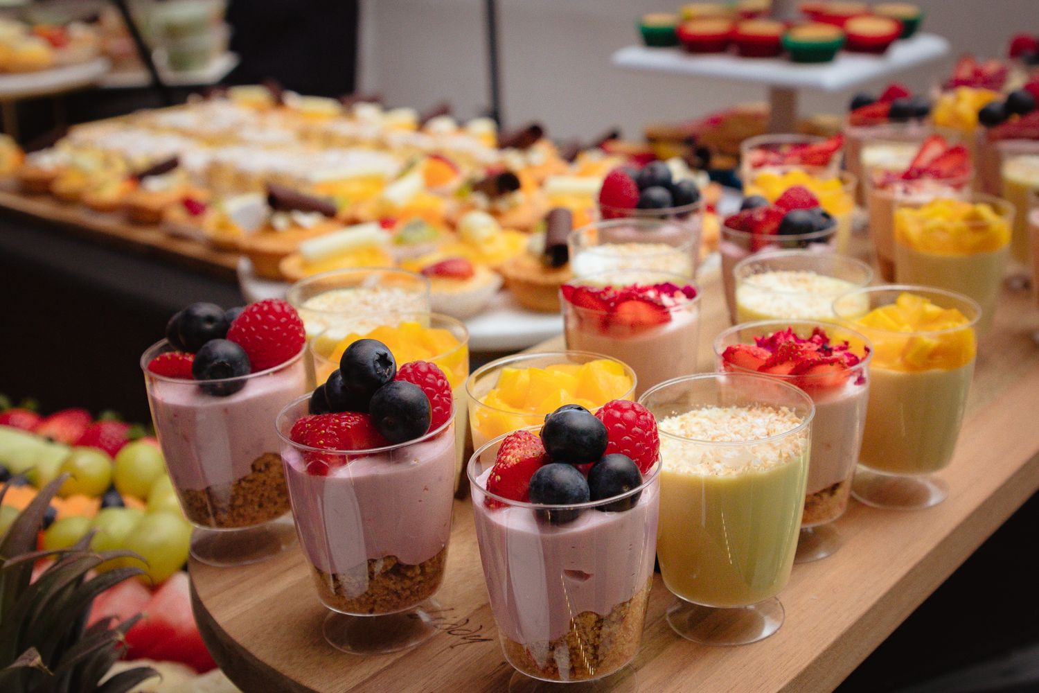 Elegant dessert display featuring colorful mousses and fruit garnishes on wooden serving board.