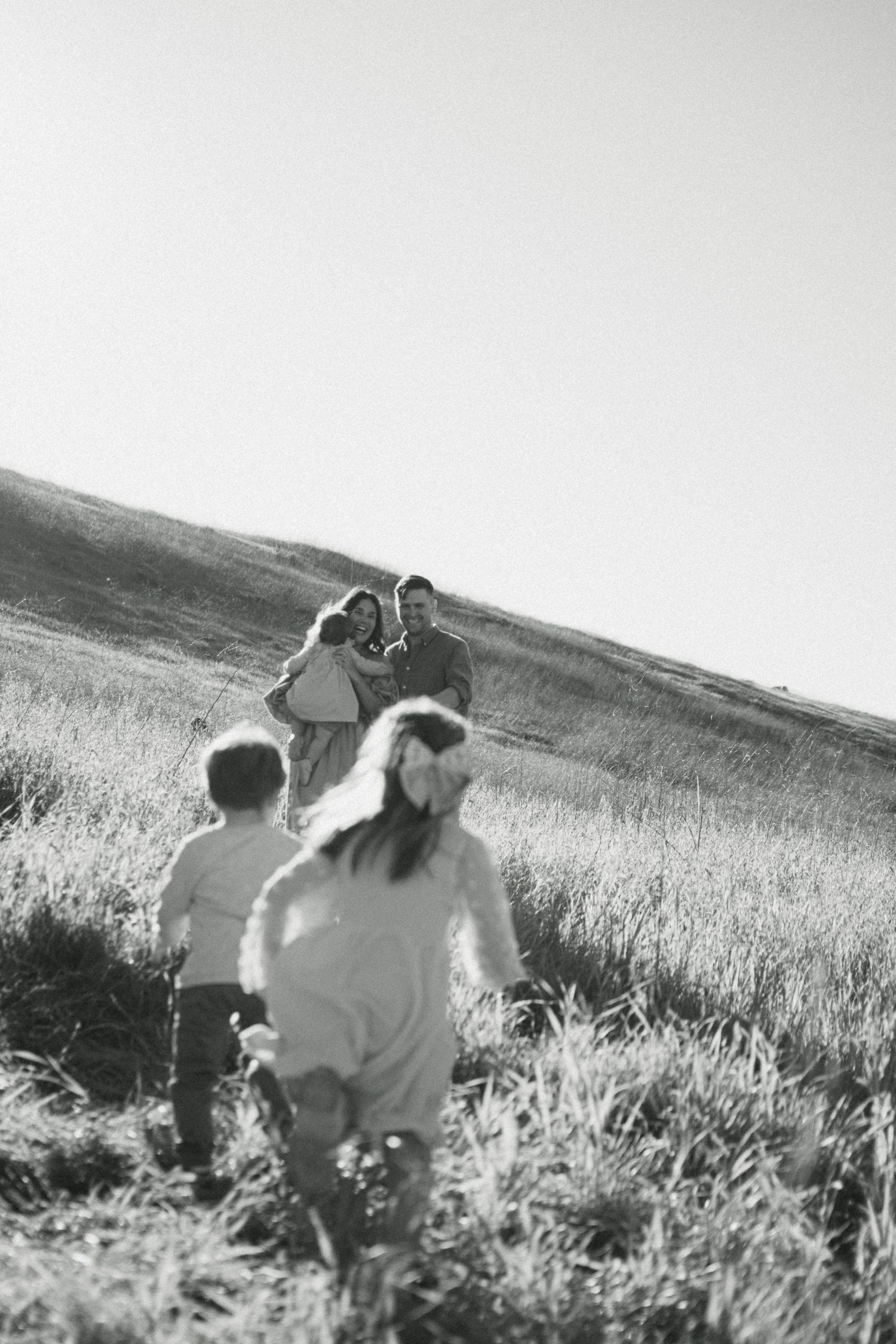 Black and white photo of a family with two children running through an open grassy hillside.